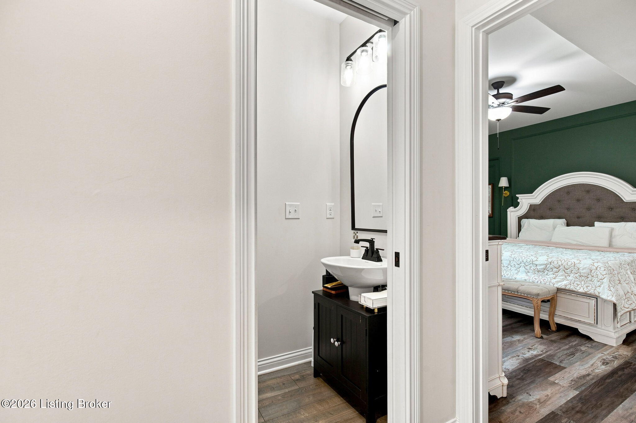 Bathroom vanity with an arched mirror beside a bedroom with a white bed and dark green wall.