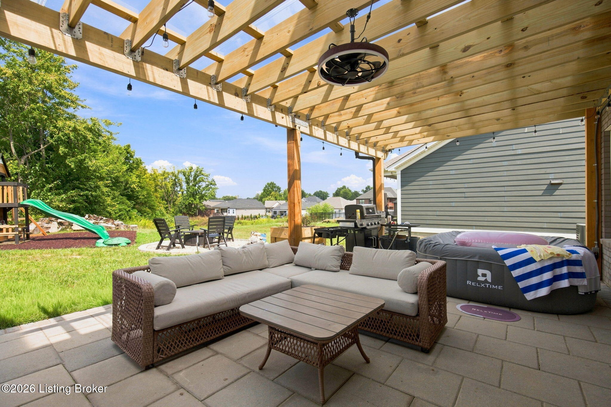 Furnished patio under a timber pergola with a sectional, grill, and inflatable hot tub.