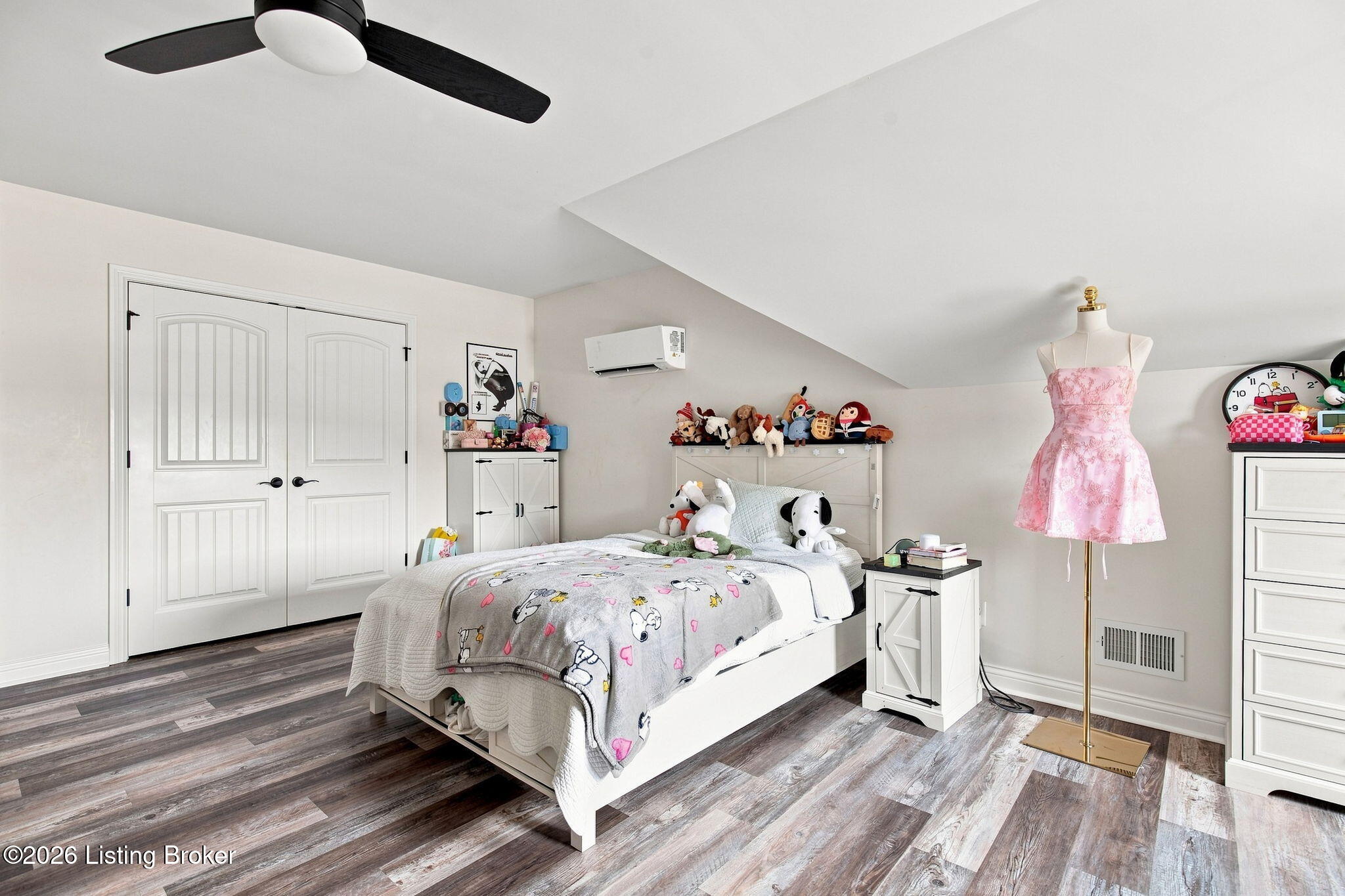 Bedroom with Snoopy-patterned bedding, stuffed toys, and a pink dress on a mannequin.