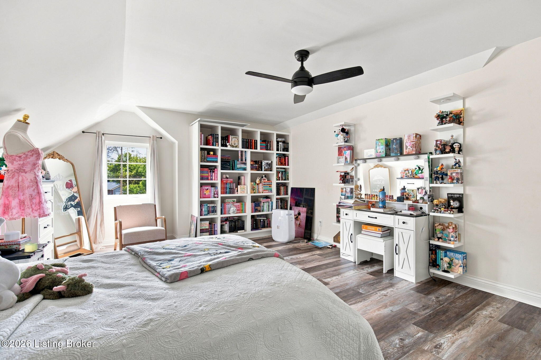 Bright bedroom with a large bed, built-in bookshelves, and a white desk with collectible displays.