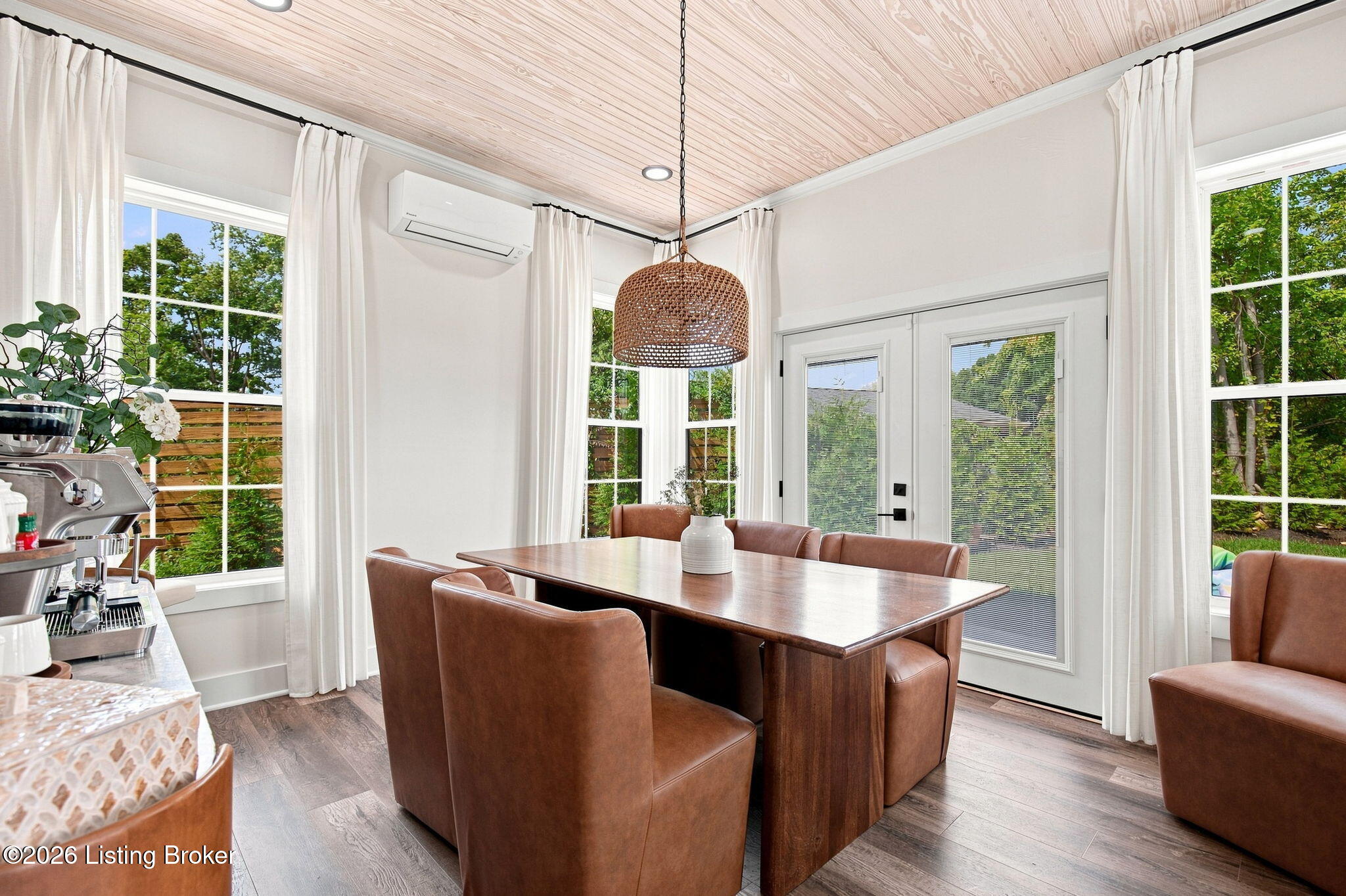 Dining room with a wood table, brown chairs, tall windows, and a woven pendant light.