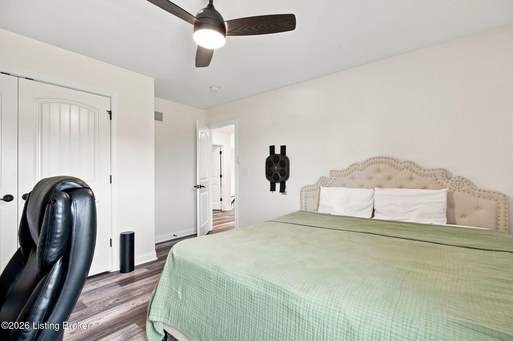 Bedroom with a pale green quilt, tufted headboard, dark ceiling fan, and wood-look flooring.