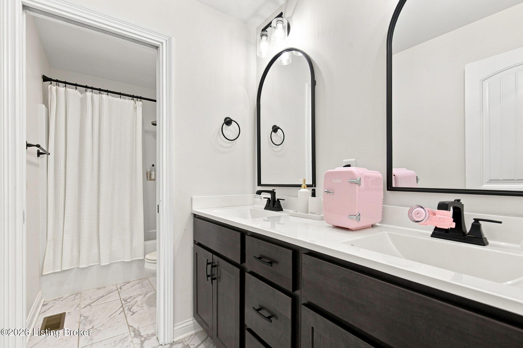 Bathroom with dark double vanity, arched mirrors, and a curtained shower.