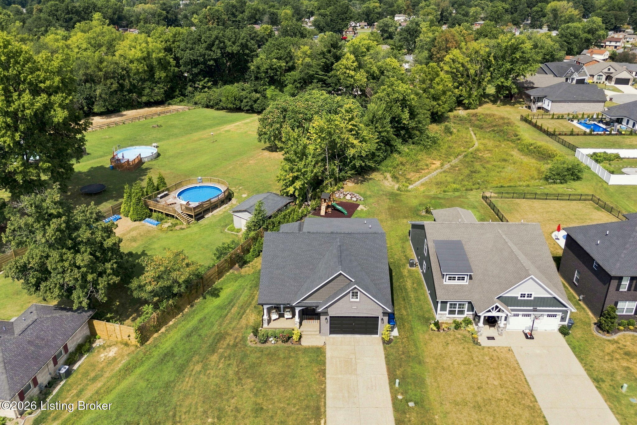 Aerial view of a home with a spacious tree-lined backyard, two pools, and a playset.