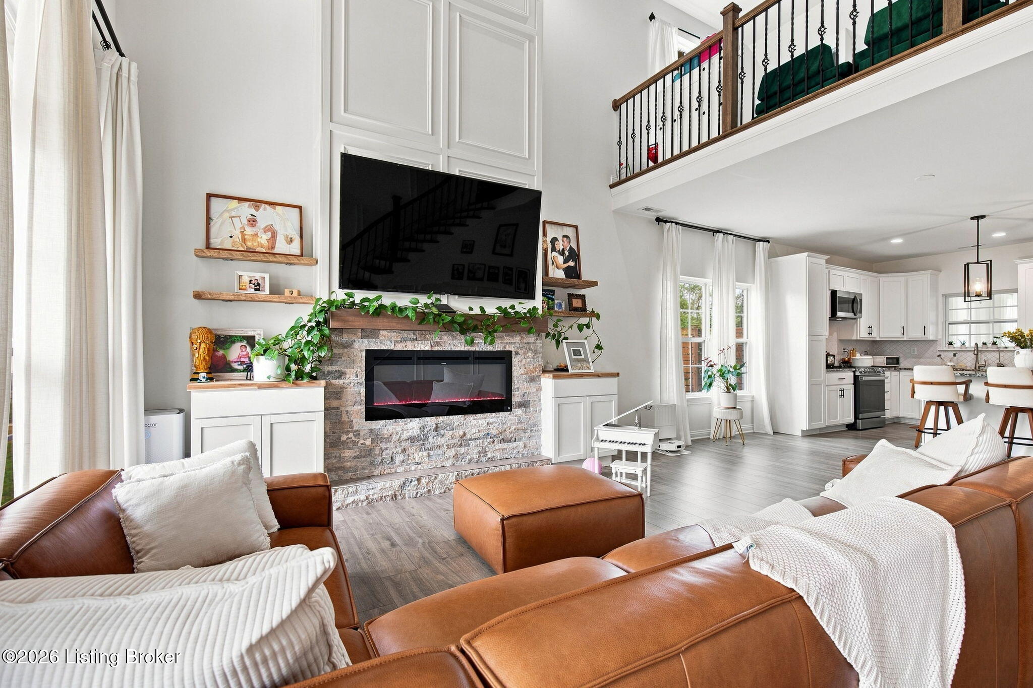 Furnished living room with vaulted ceiling, stone fireplace, leather sofas, and open kitchen.