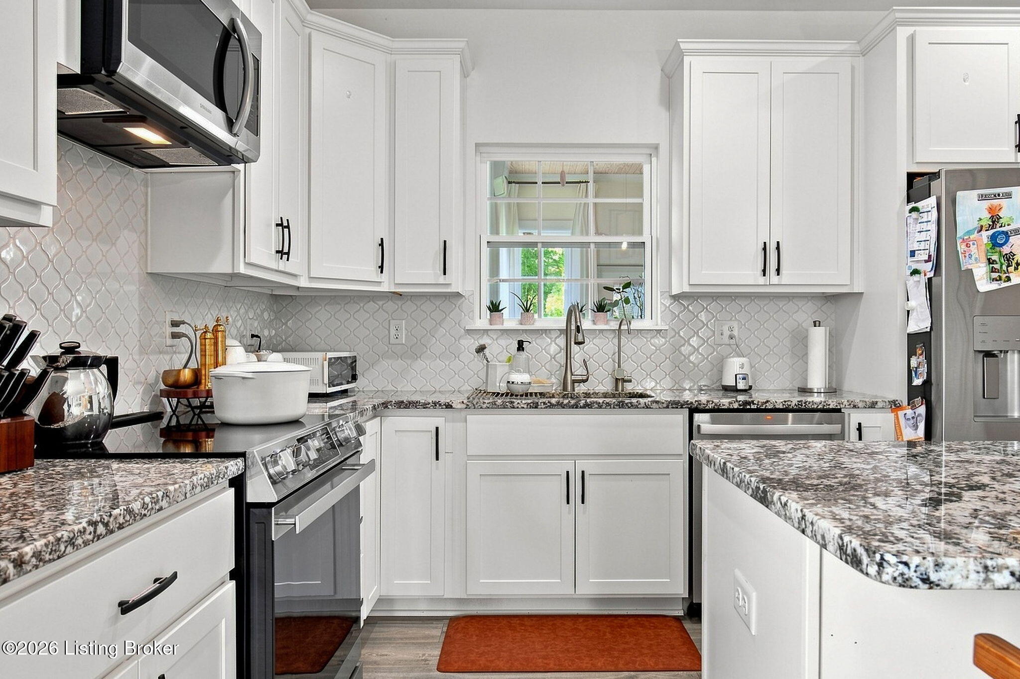 Kitchen with white shaker cabinets, patterned backsplash, granite counters, and stainless steel appliances.