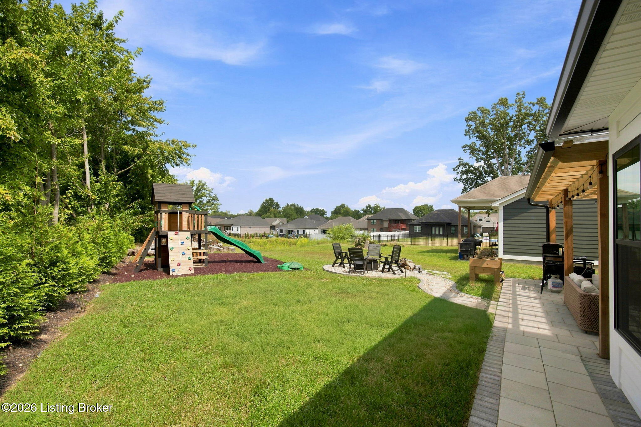 Backyard with a wooden playset, wide lawn, outdoor dining area, and covered patio.