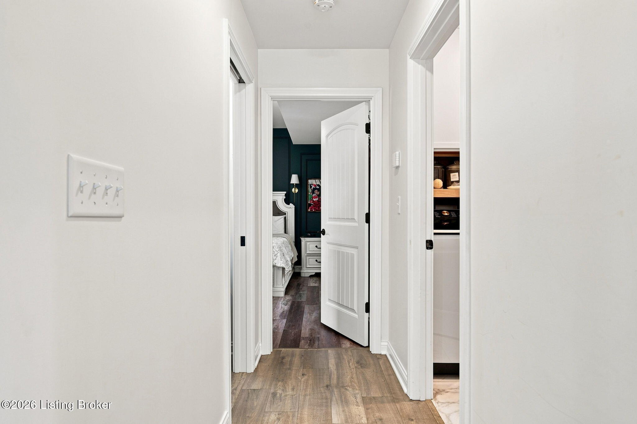 Hallway with wood-look floors and an open doorway to a bedroom with a dark teal wall.