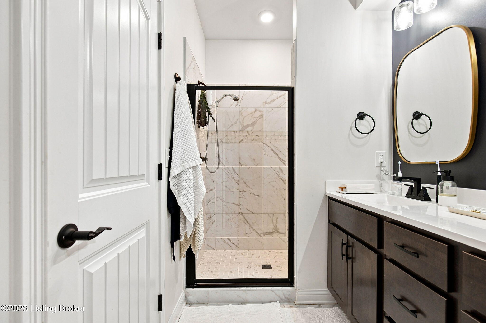 Bathroom with a marble-look tiled shower, black-framed glass, and dark wood vanity.