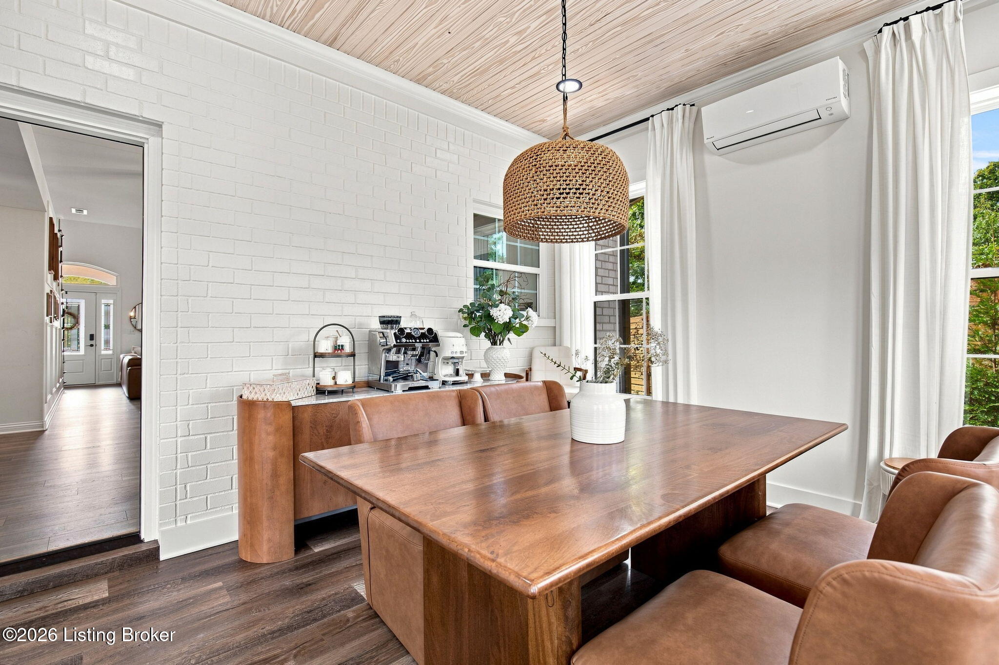 Dining area with a large wooden table, tan leather seating, and a woven pendant light.