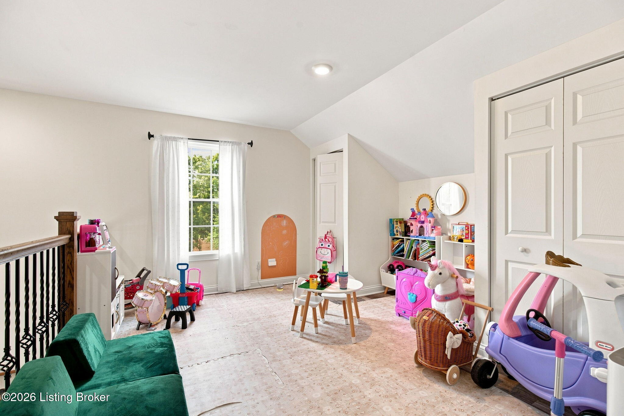 Children’s playroom with a sloped ceiling, toy shelves, drum set, green sofa, and purple ride-on car.