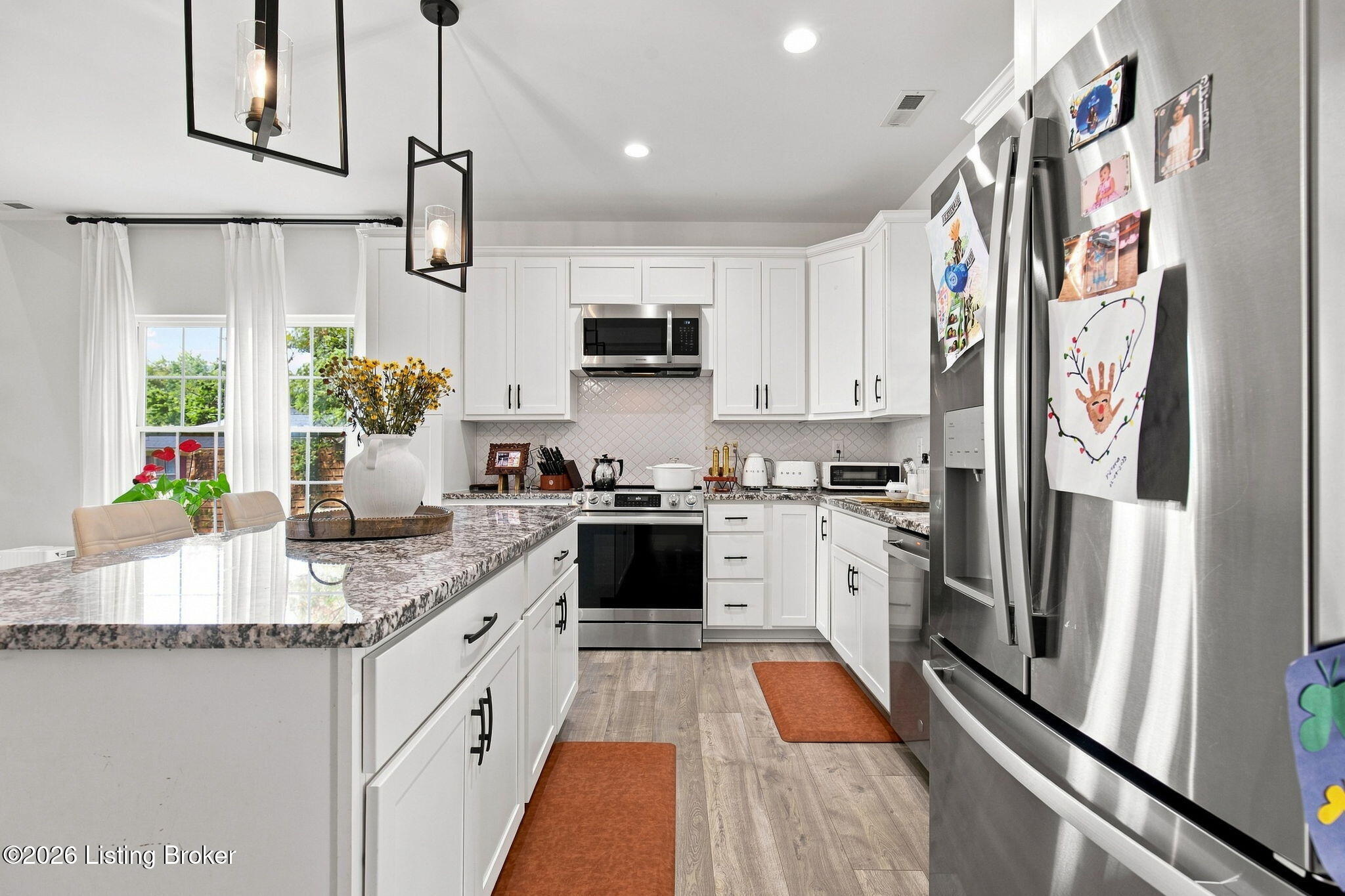 Bright kitchen with white cabinets, stainless steel appliances, and a large stone-topped island.