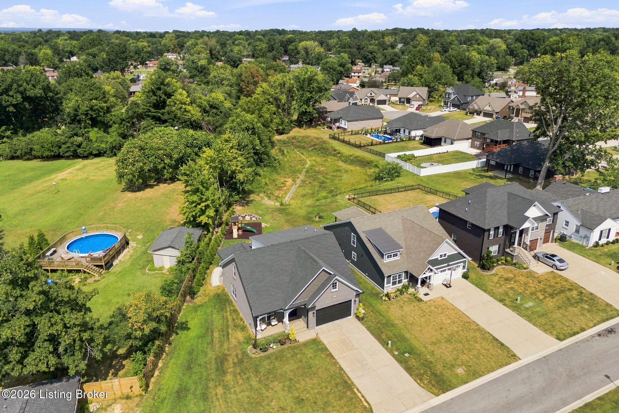 Aerial view of neighborhood homes beside a grassy open area and a fenced above-ground pool.