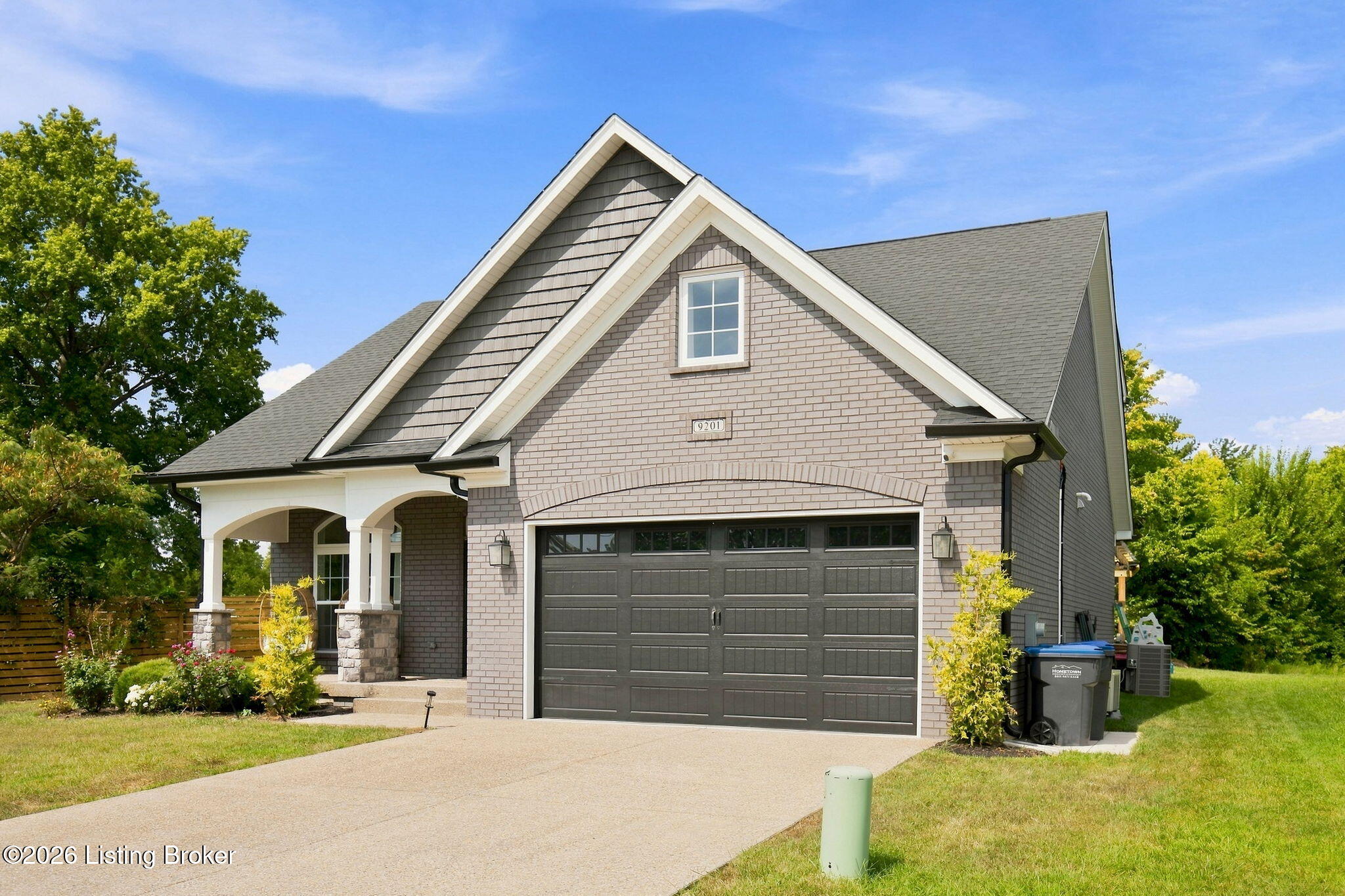 Gray-brick home with steep gables, a covered porch, and a dark double garage door.