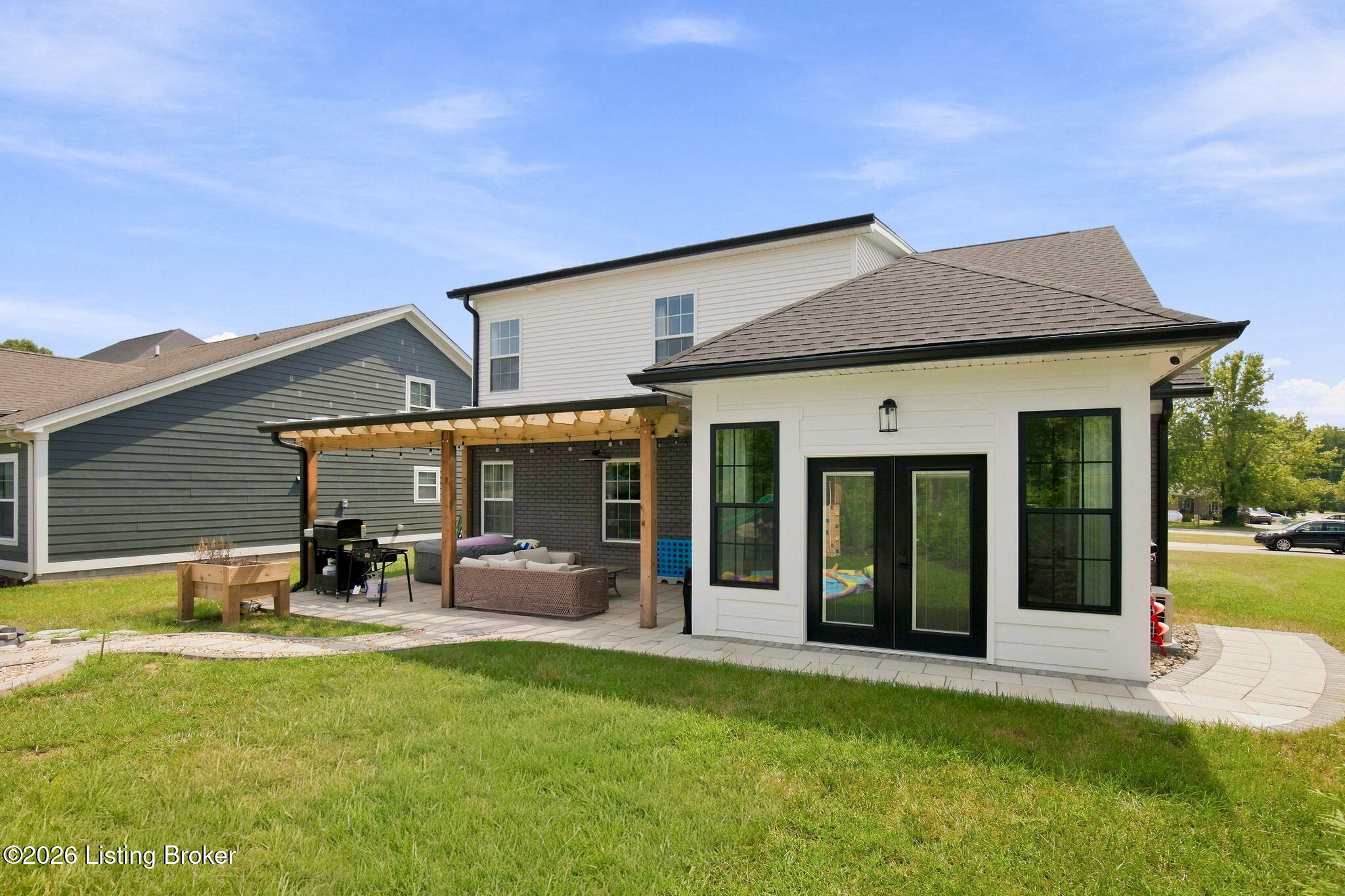 Rear of a white two-story house with a pergola-covered patio, outdoor seating, and a broad lawn.