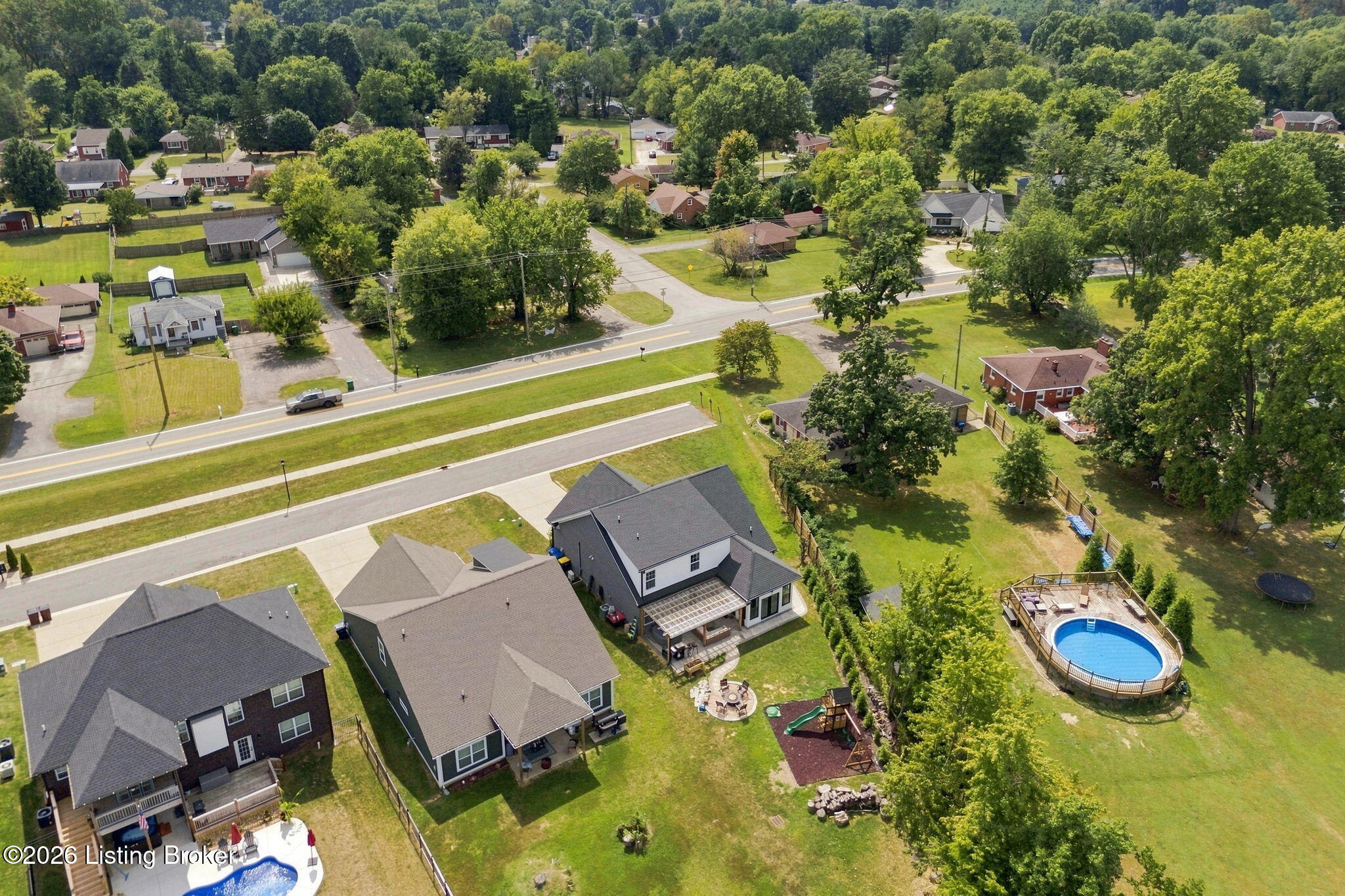 Aerial view of a home and neighboring yards, with a pergola and play area in a fenced backyard.