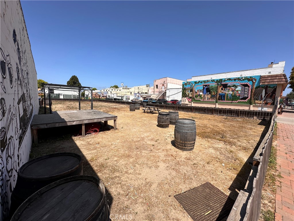Outdoor courtyard with wooden barrels, a raised platform, and a colorful mural wall.