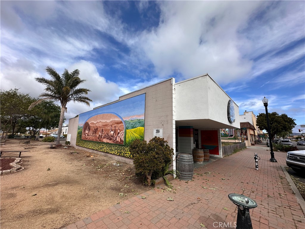 Commercial building with a colorful landscape mural beside a brick sidewalk and palm tree.