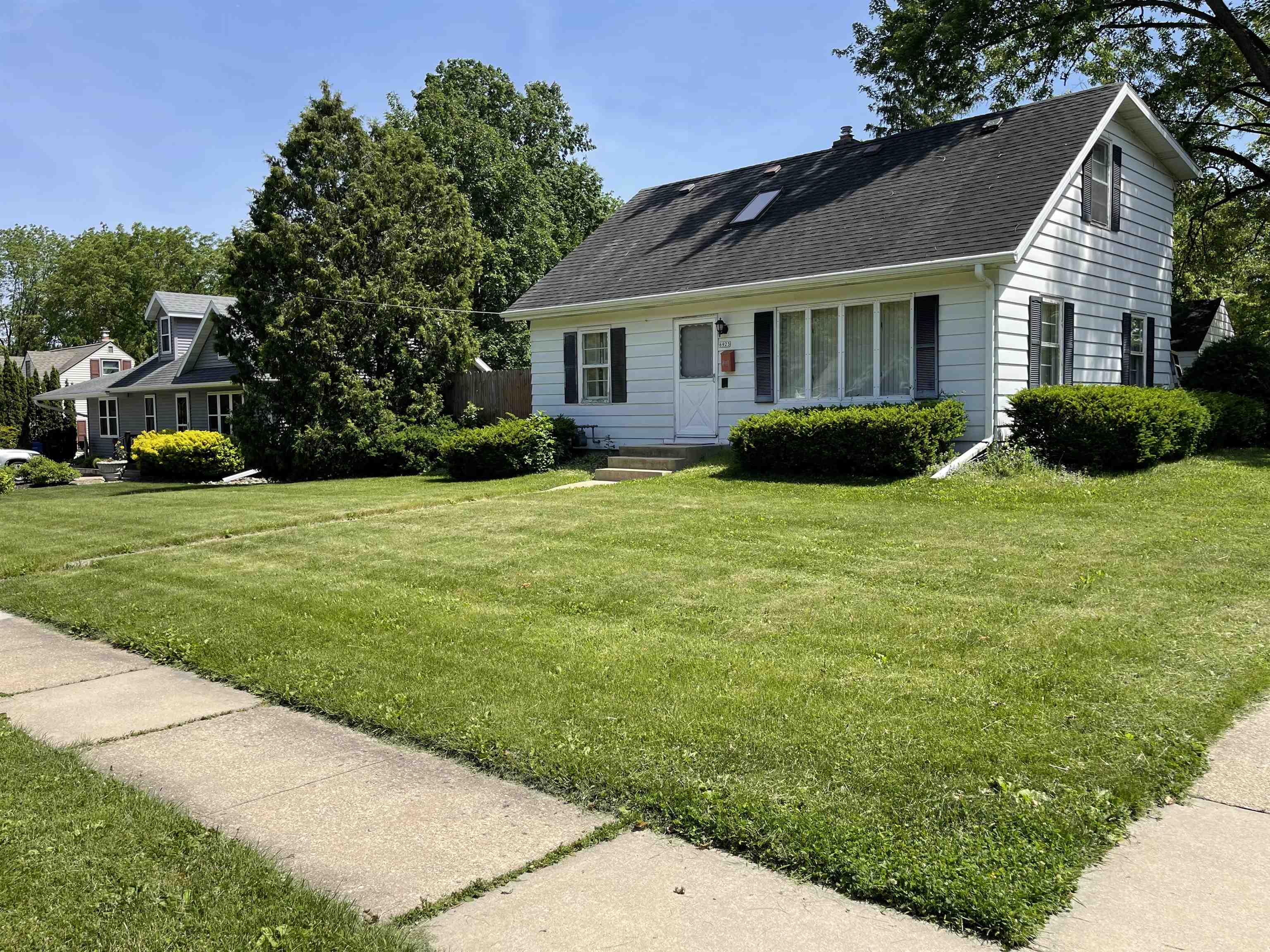 White two-story house with black shutters and a skylight, fronted by shrubs and a broad lawn.