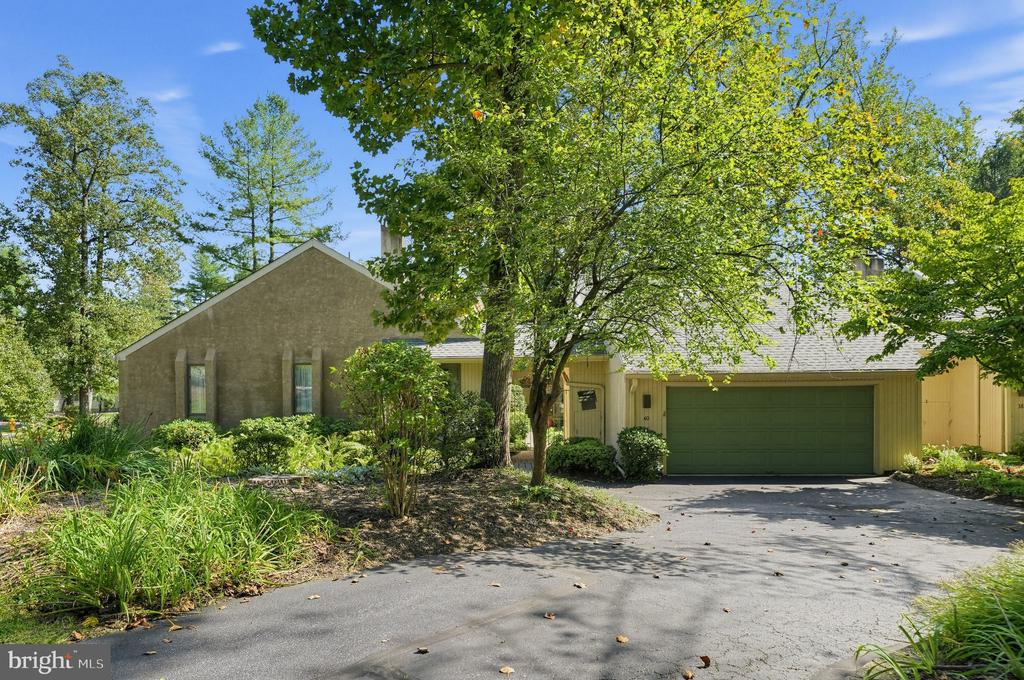 House with green double garage door, shaded by mature trees beside a landscaped driveway.