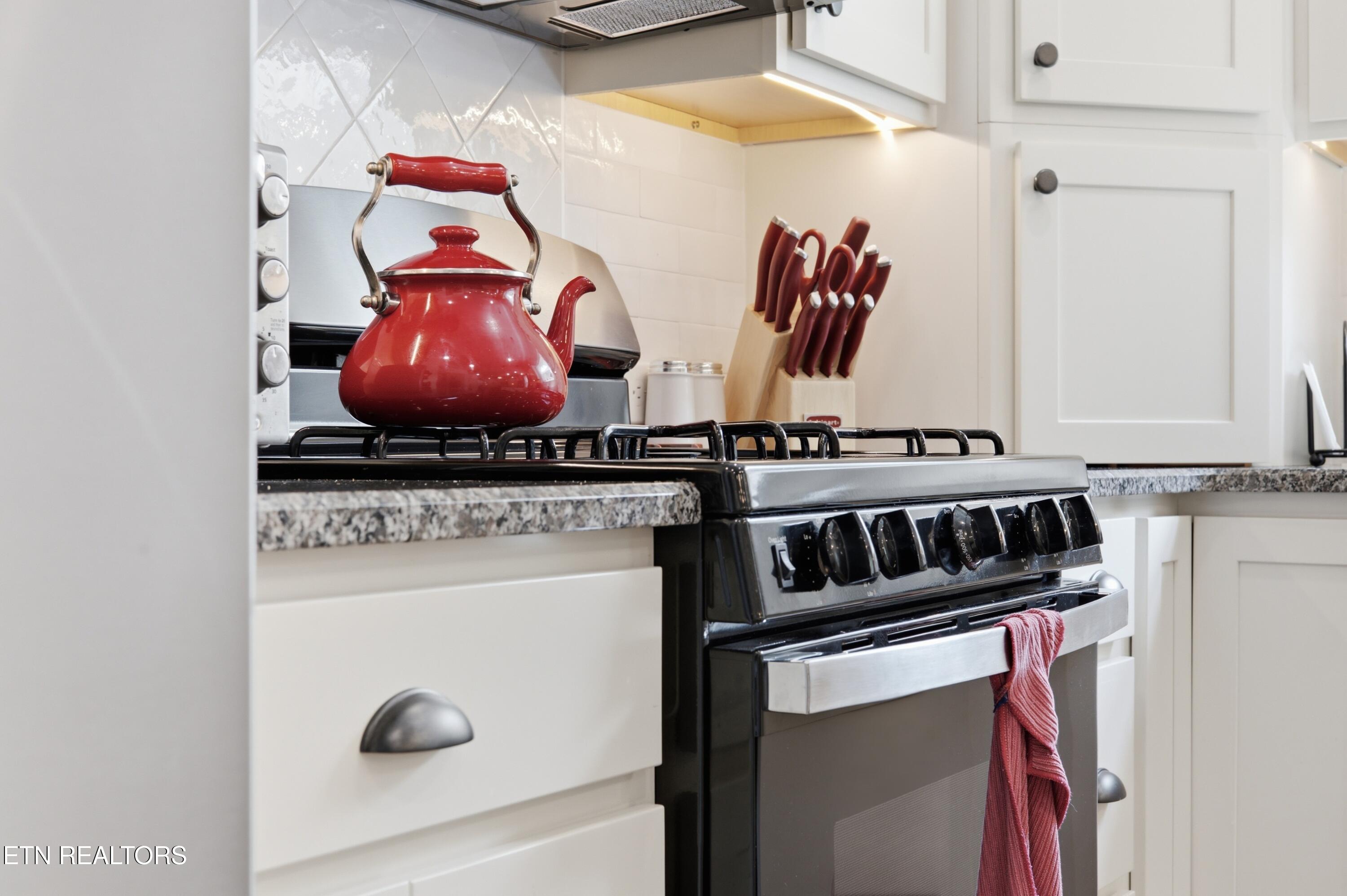 Kitchen range with a red kettle, knife block, and red towel against white cabinetry.