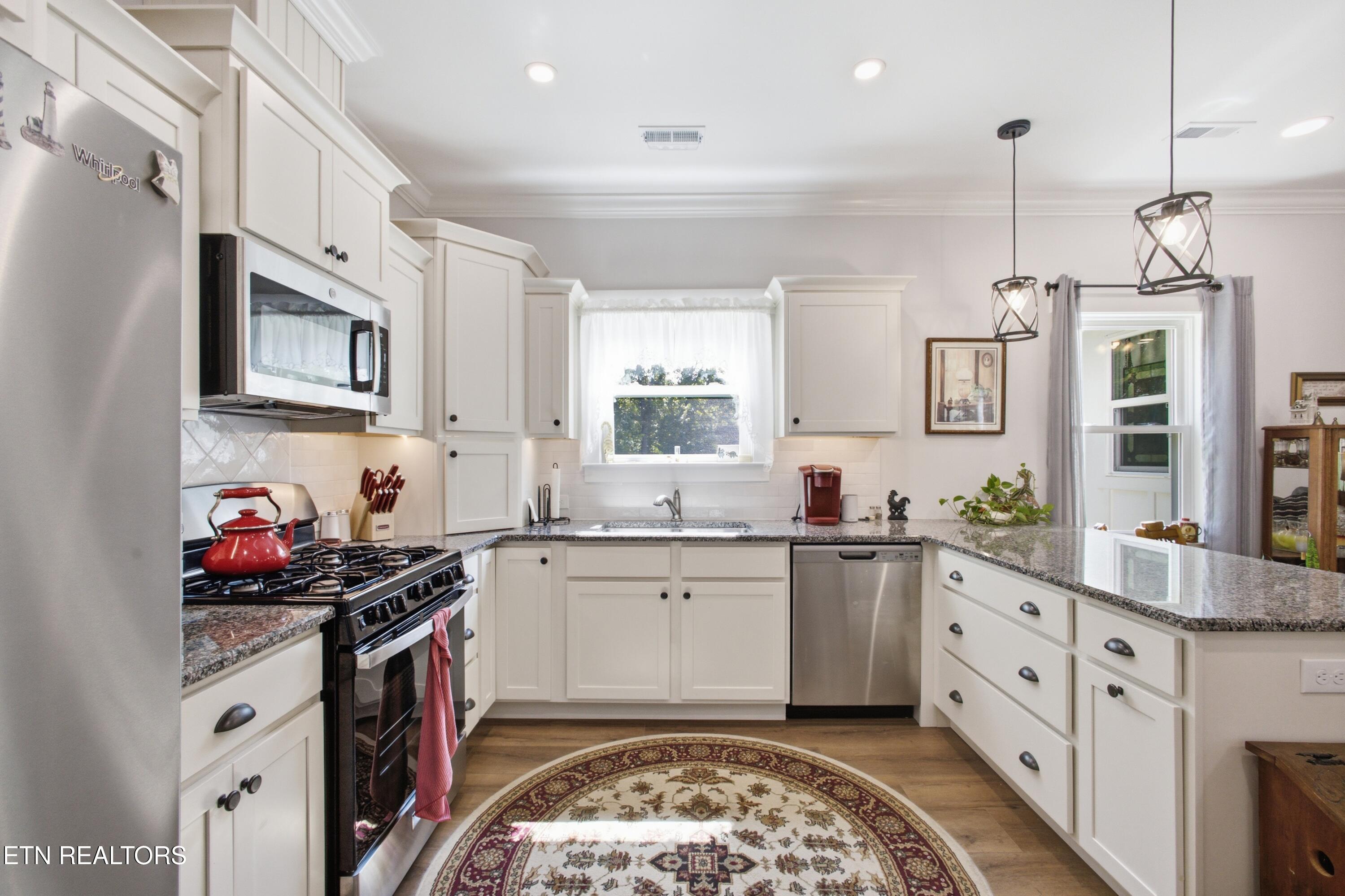 Bright kitchen with white cabinets, granite counters, stainless steel appliances, and a patterned oval rug.