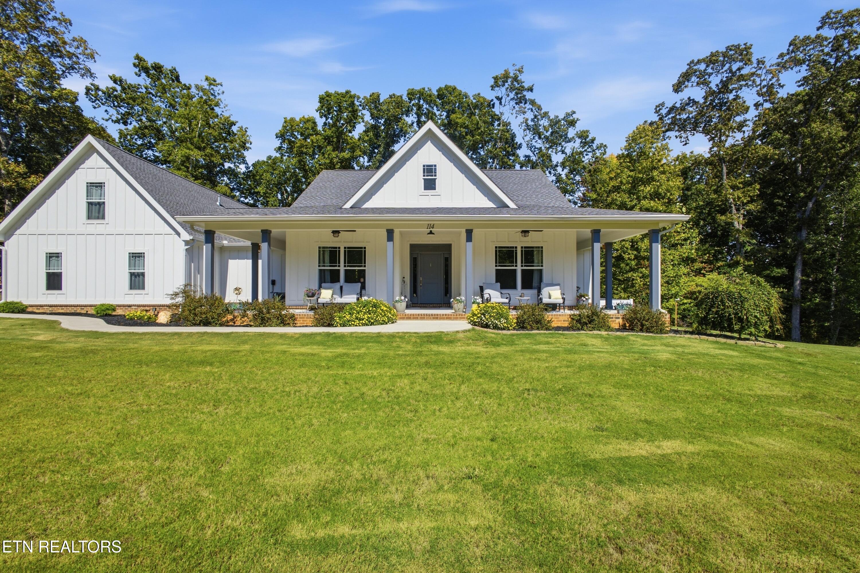 White gabled home with a covered front porch, landscaped beds, and a broad green lawn.