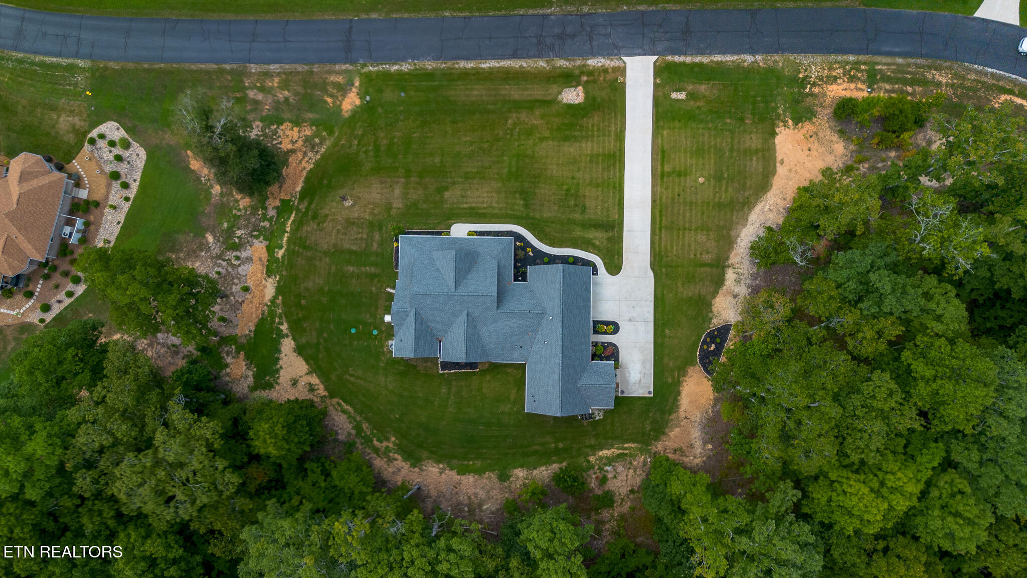 Aerial view of a home with a broad lawn, long driveway, and surrounding trees.