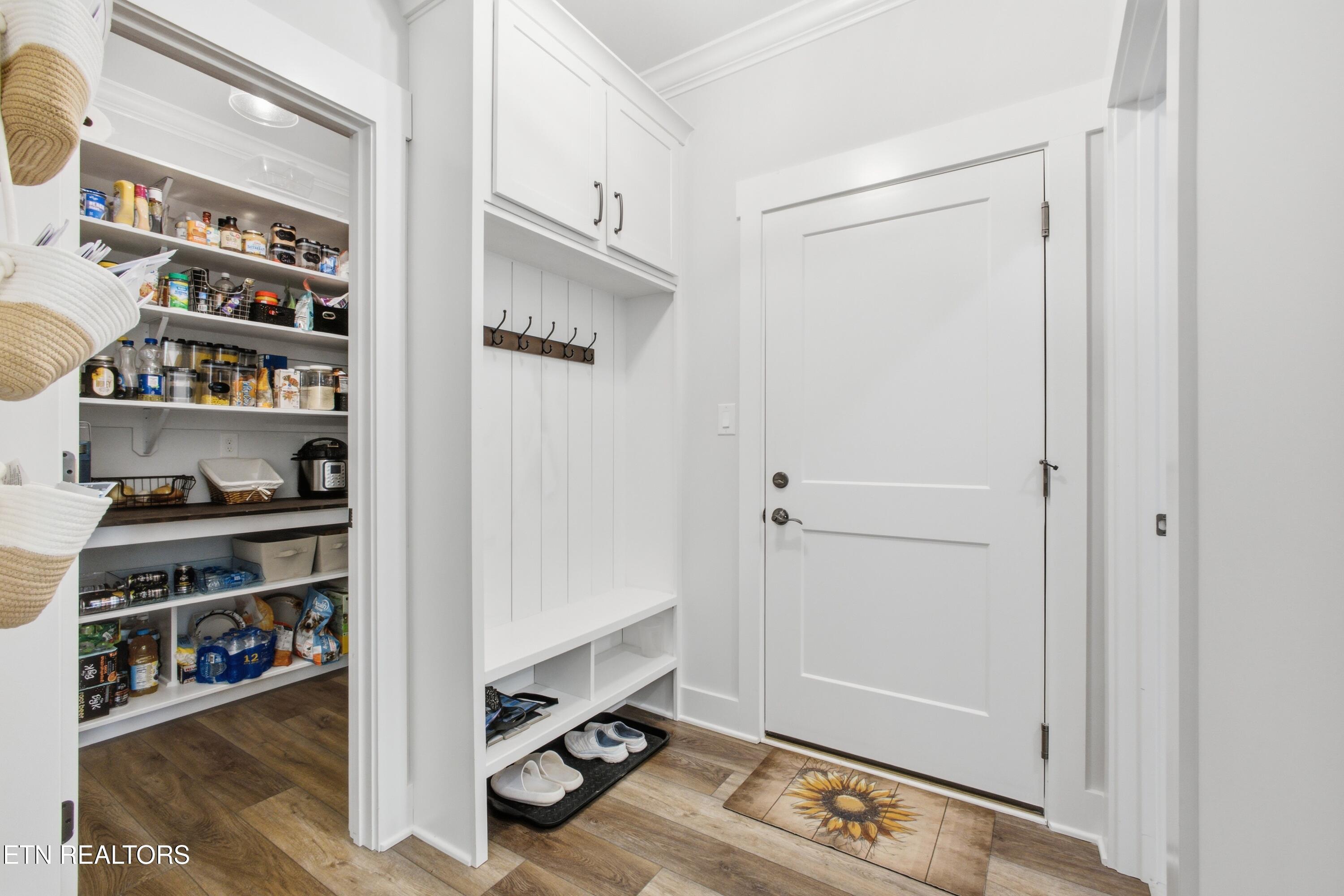 Entryway with built-in mudroom bench and hooks beside an open pantry.