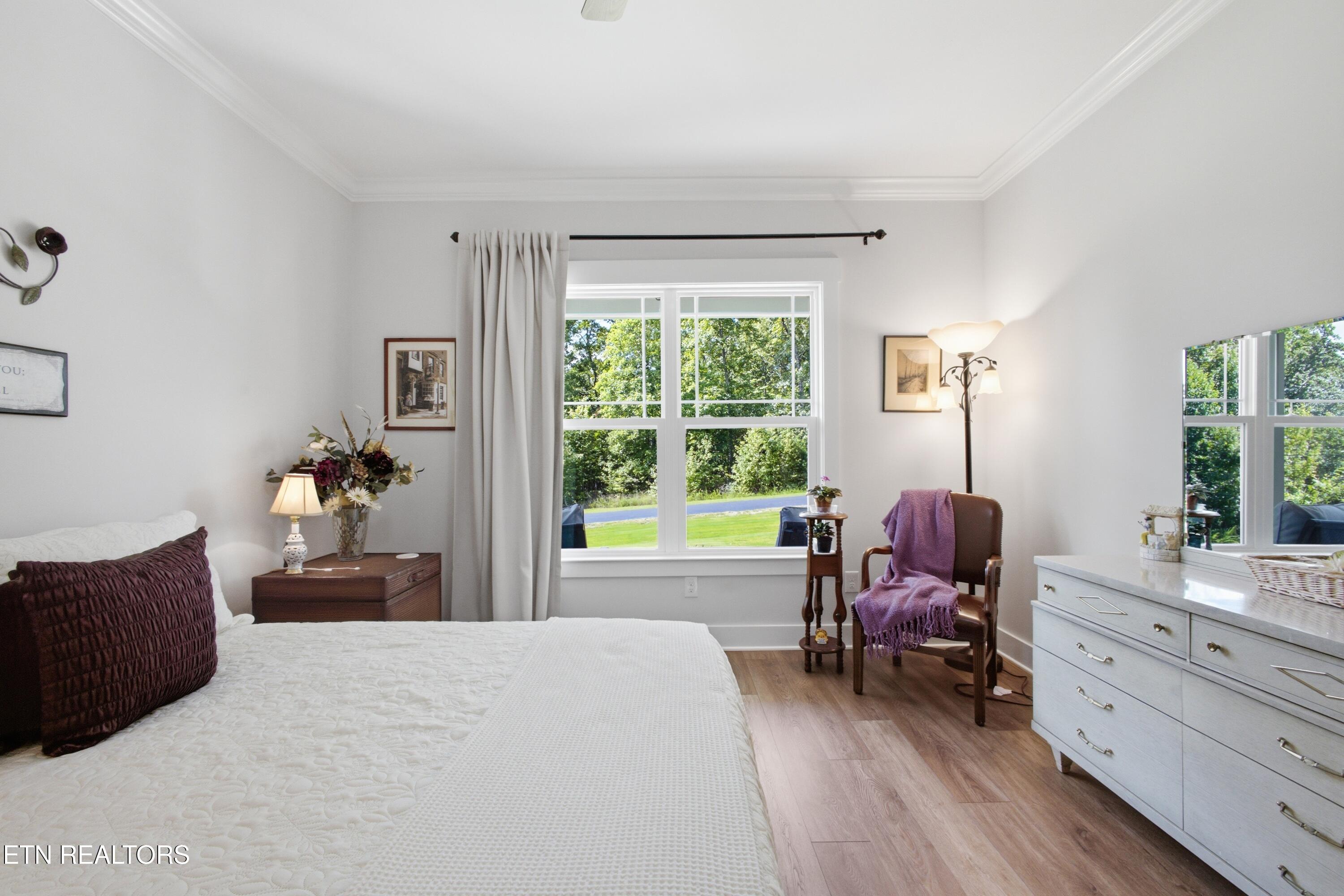 Bedroom with a white bed, large garden-facing windows, and a chair draped in purple.