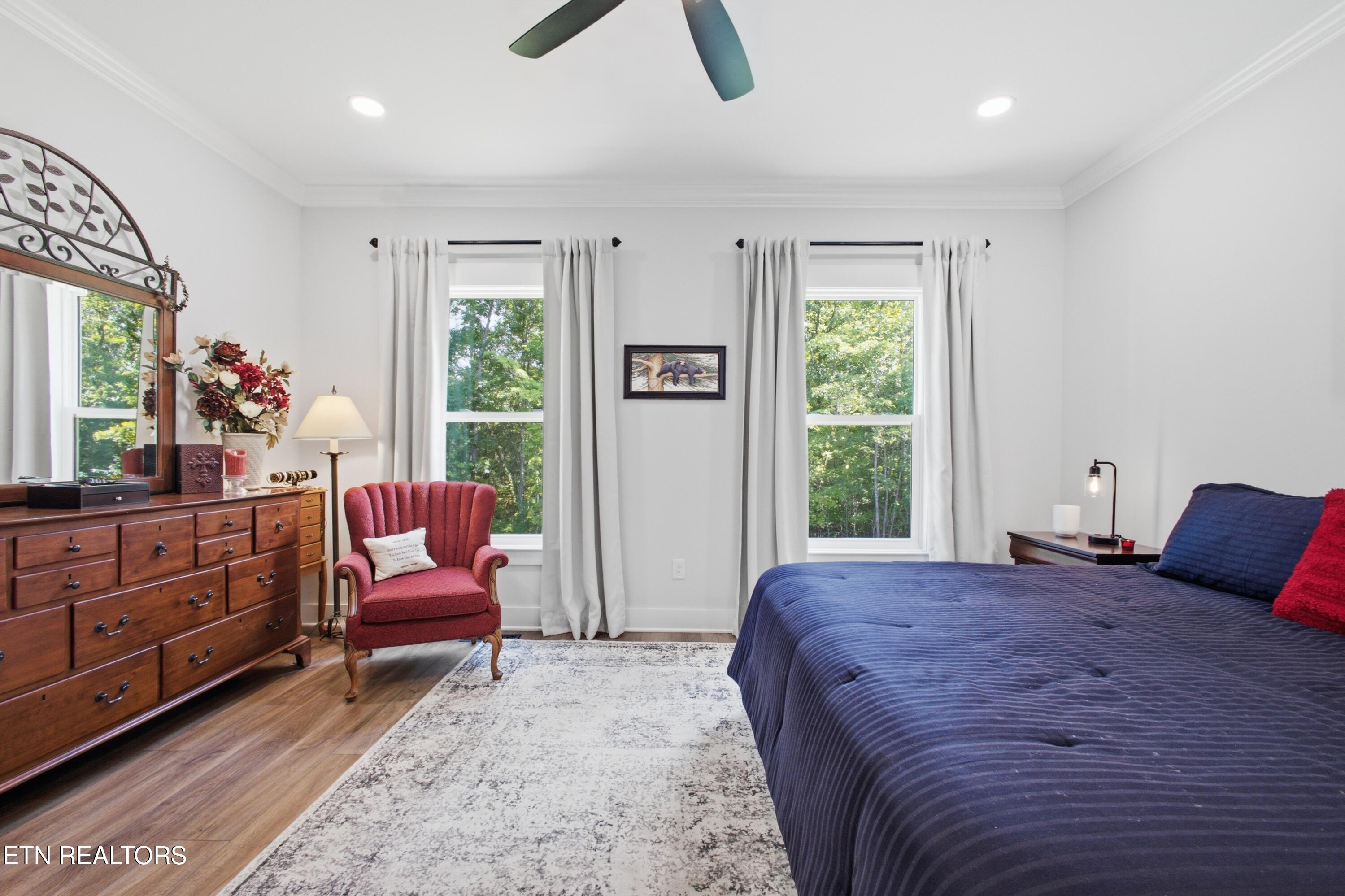 Bedroom with a navy bed, red armchair, wooden dresser and mirror, and two windows overlooking trees.