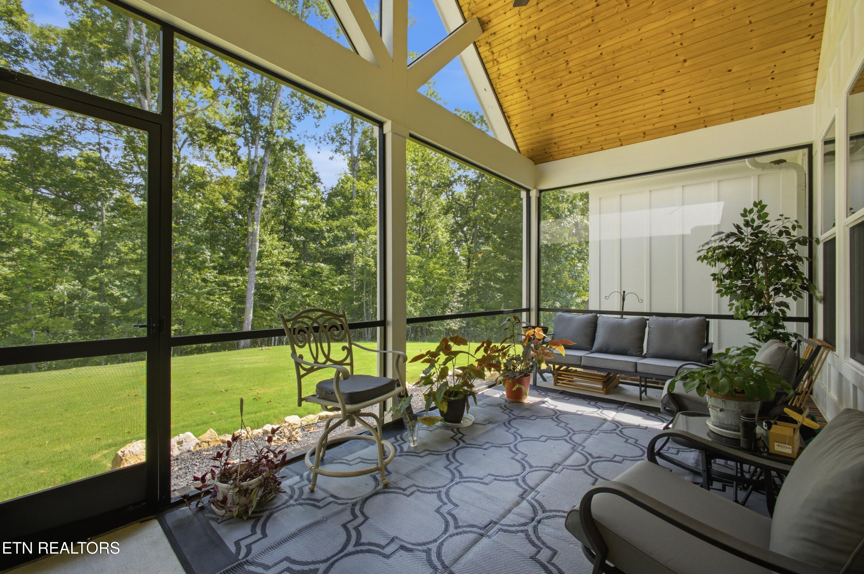 Screened porch with gray seating and a wood ceiling overlooking a lawn and trees.