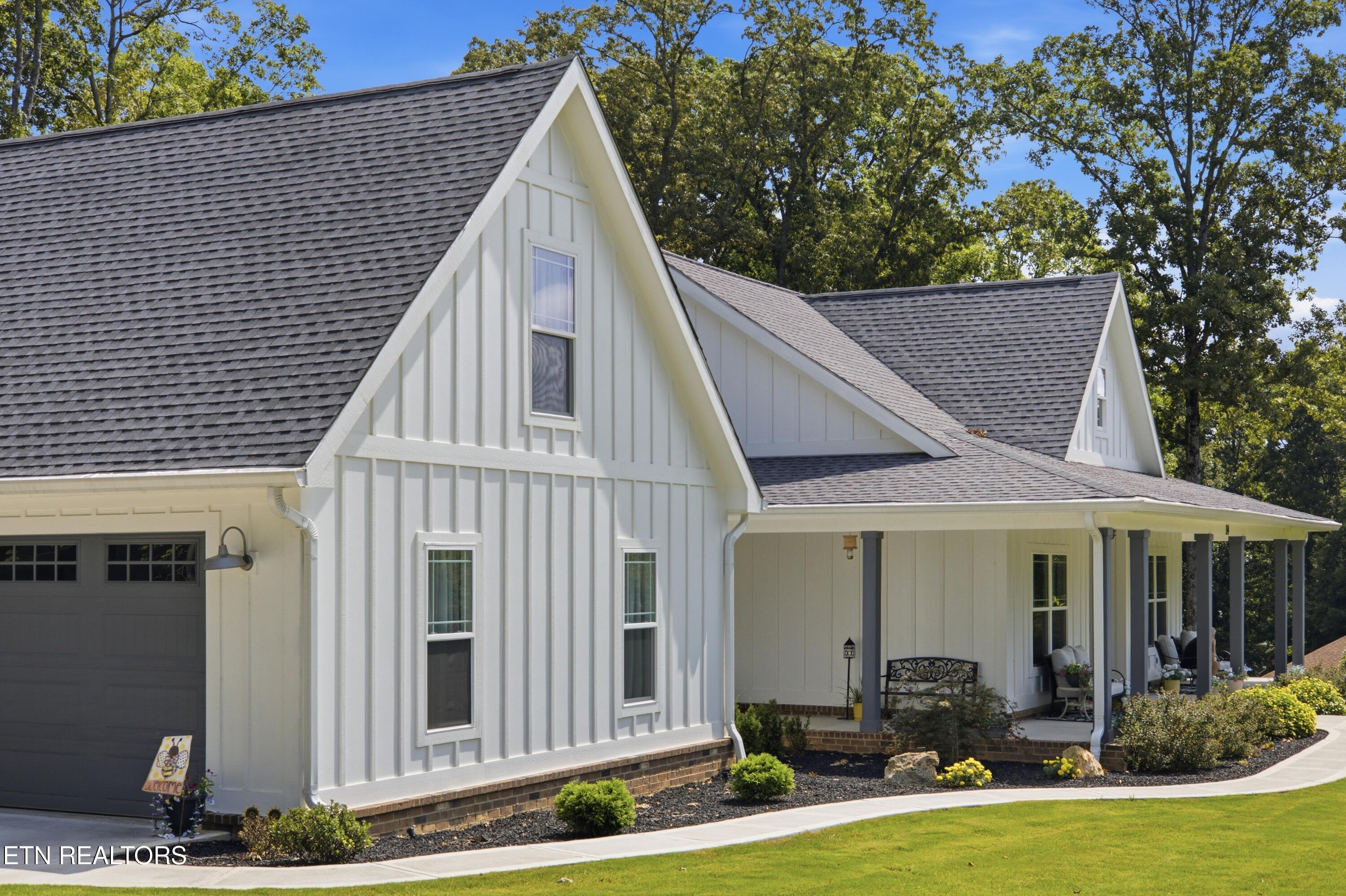 White two-story home with steep gray gables, a covered porch, attached garage, and landscaped front walkway.