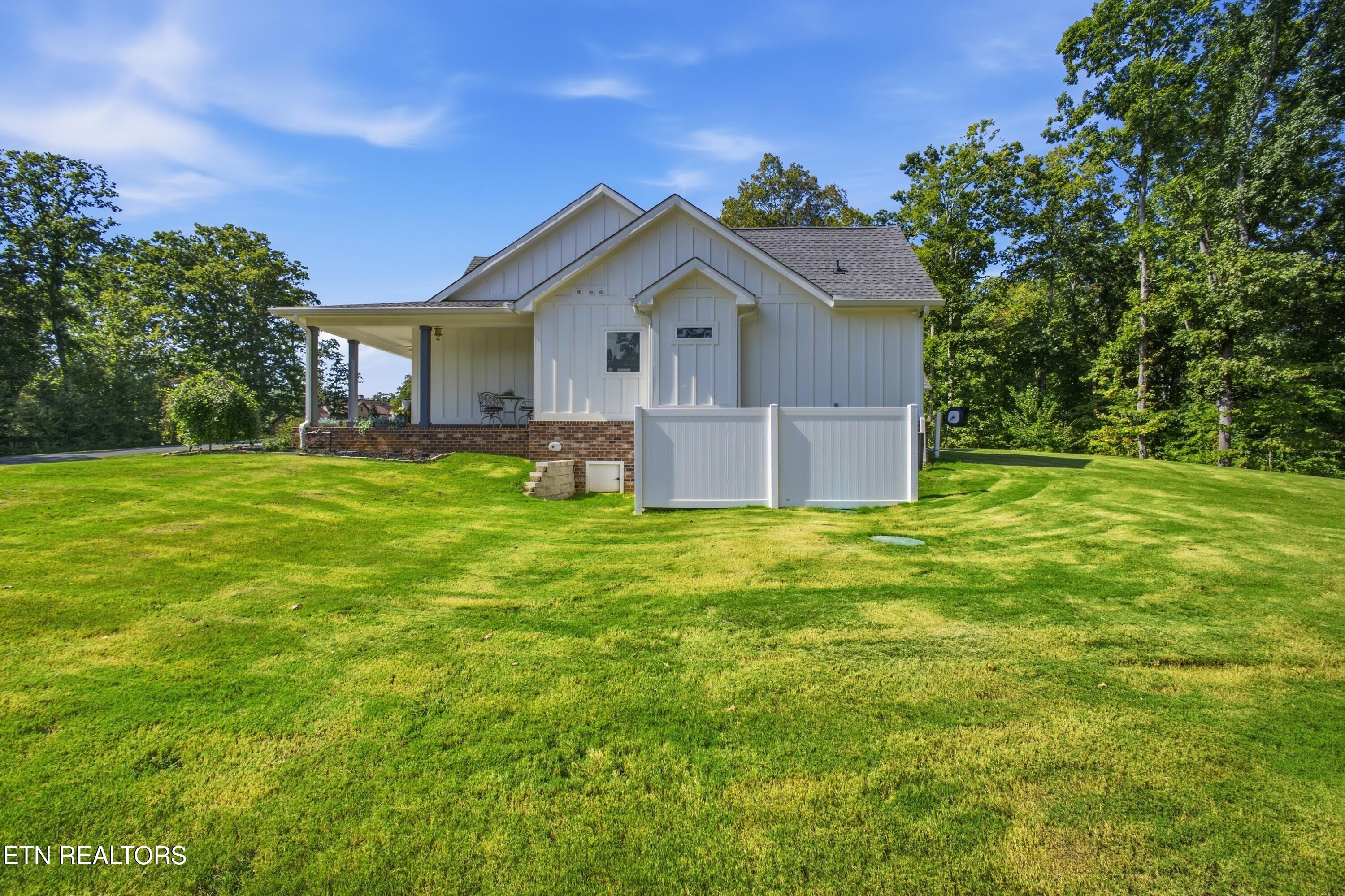 White house with a covered porch and brick foundation, set on a broad green lawn.