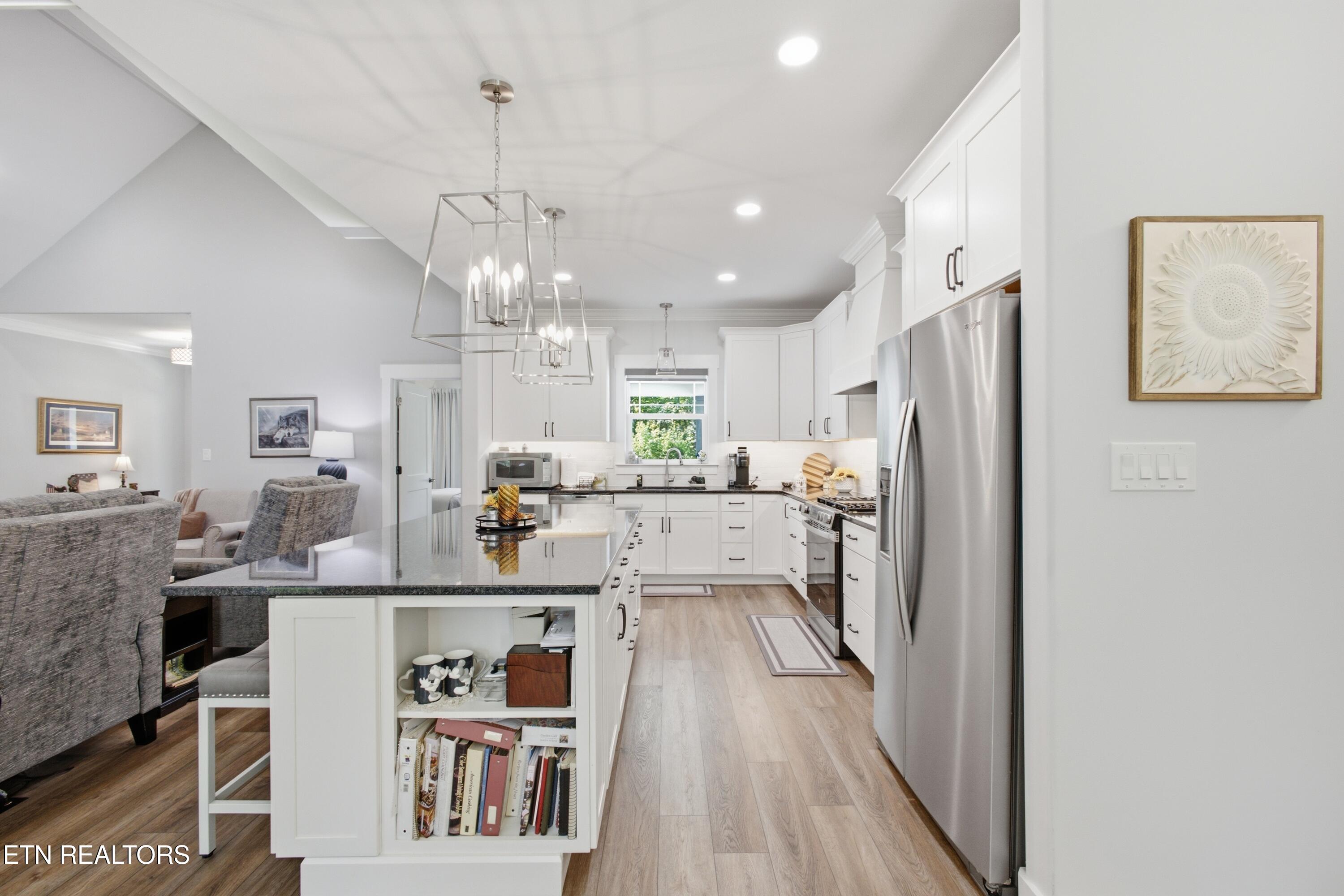 Open-plan kitchen with white cabinets, stainless steel appliances, and a large stone island beside the living area.