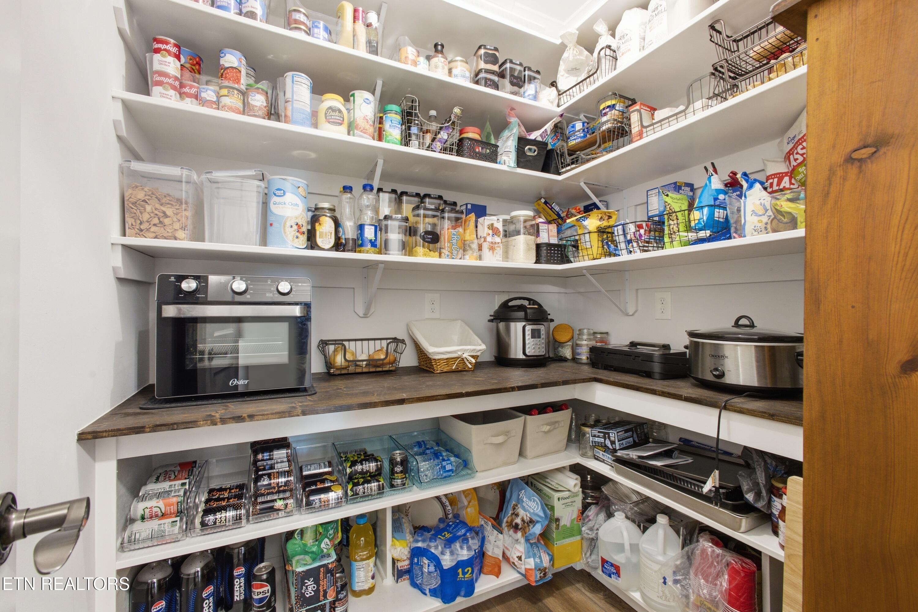 Walk-in pantry with stocked white shelves, dark wood counters, and countertop appliances.