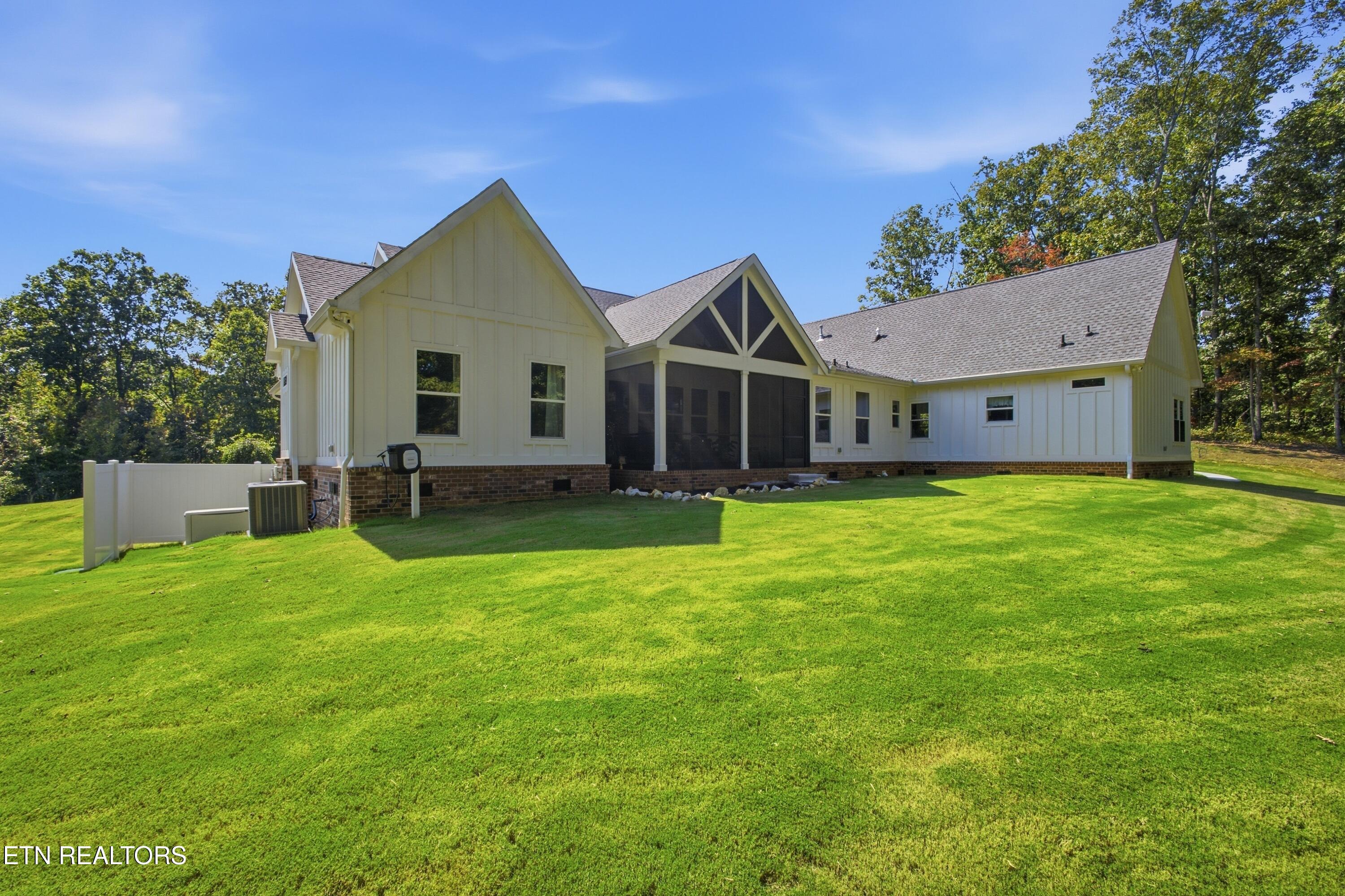 White house with a screened porch and brick foundation overlooking a broad, sloping lawn.