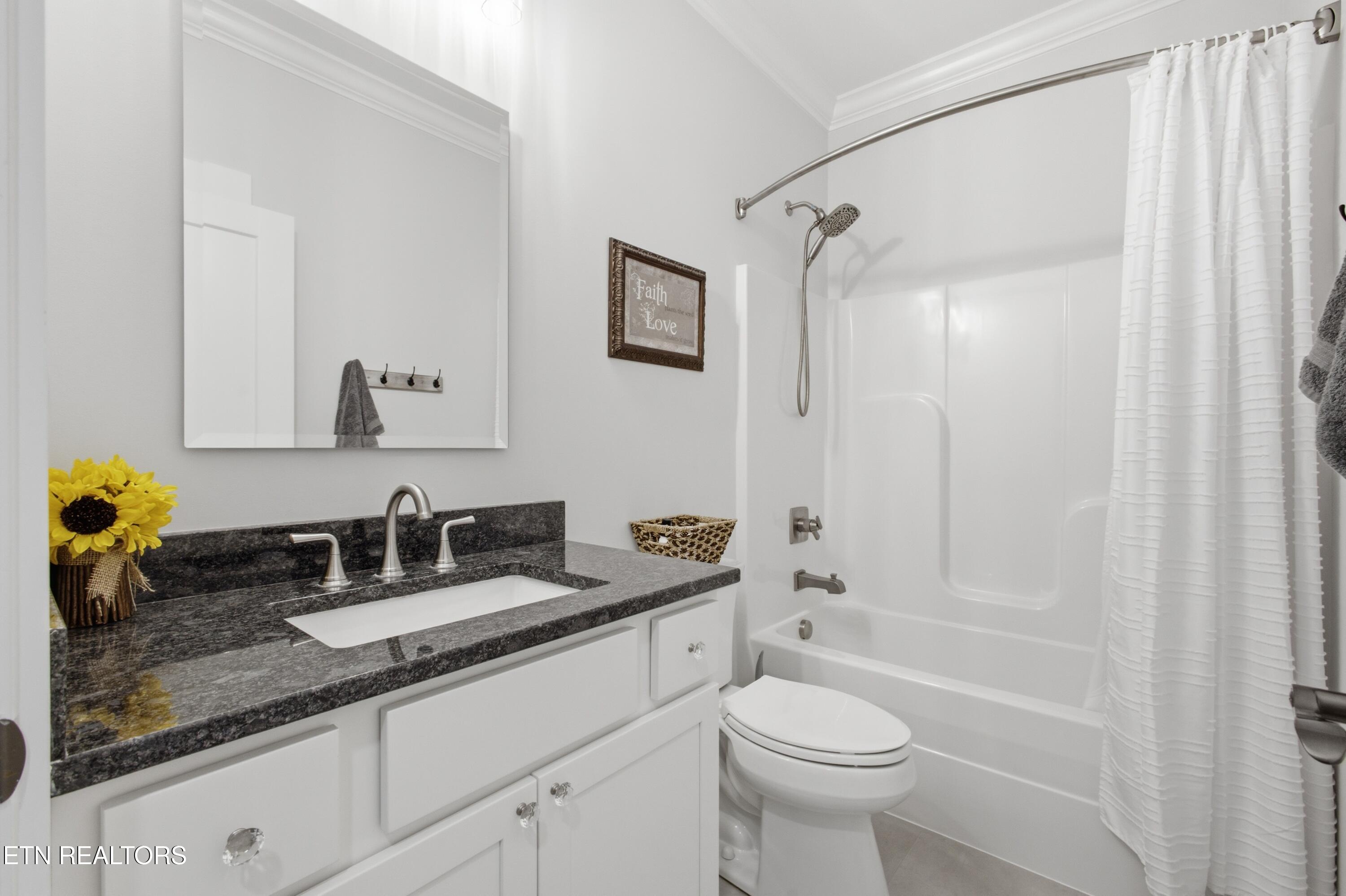 Bathroom with white vanity, dark granite countertop, and tub-shower with a white curtain.