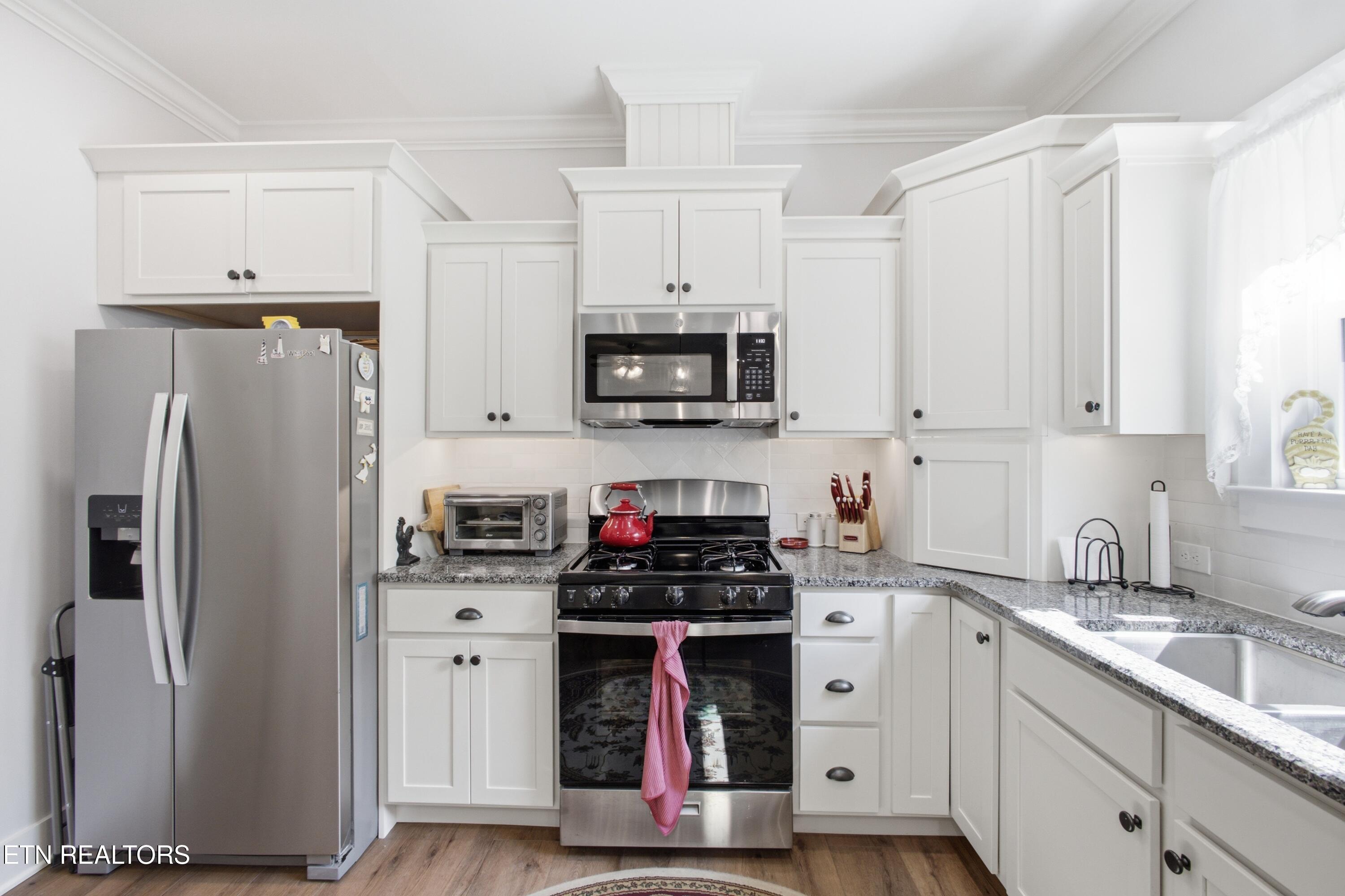 Kitchen with white cabinets, granite counters, stainless appliances, and a black gas range with a red kettle.
