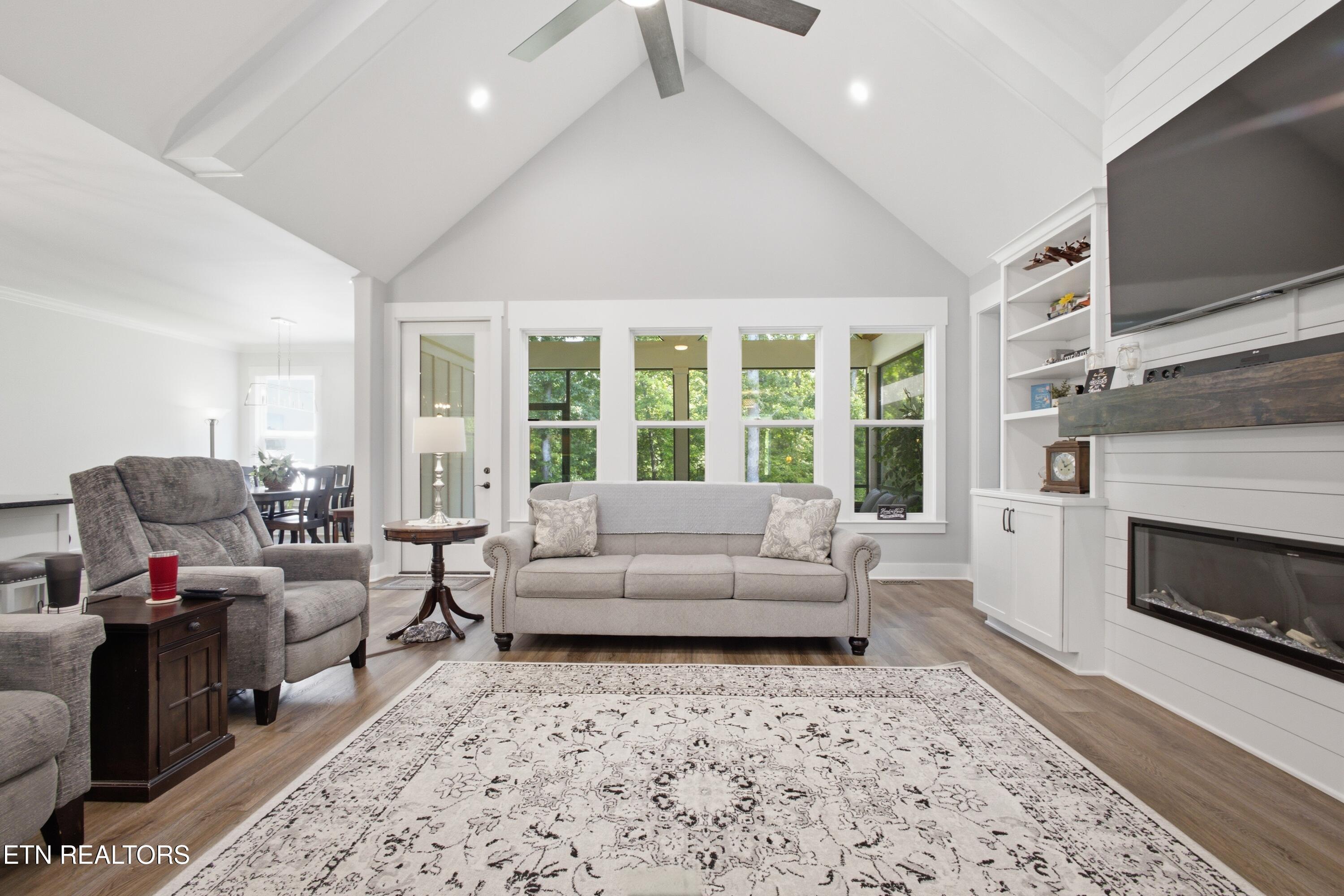 Living room with vaulted ceiling, large windows, and a built-in fireplace and TV wall.