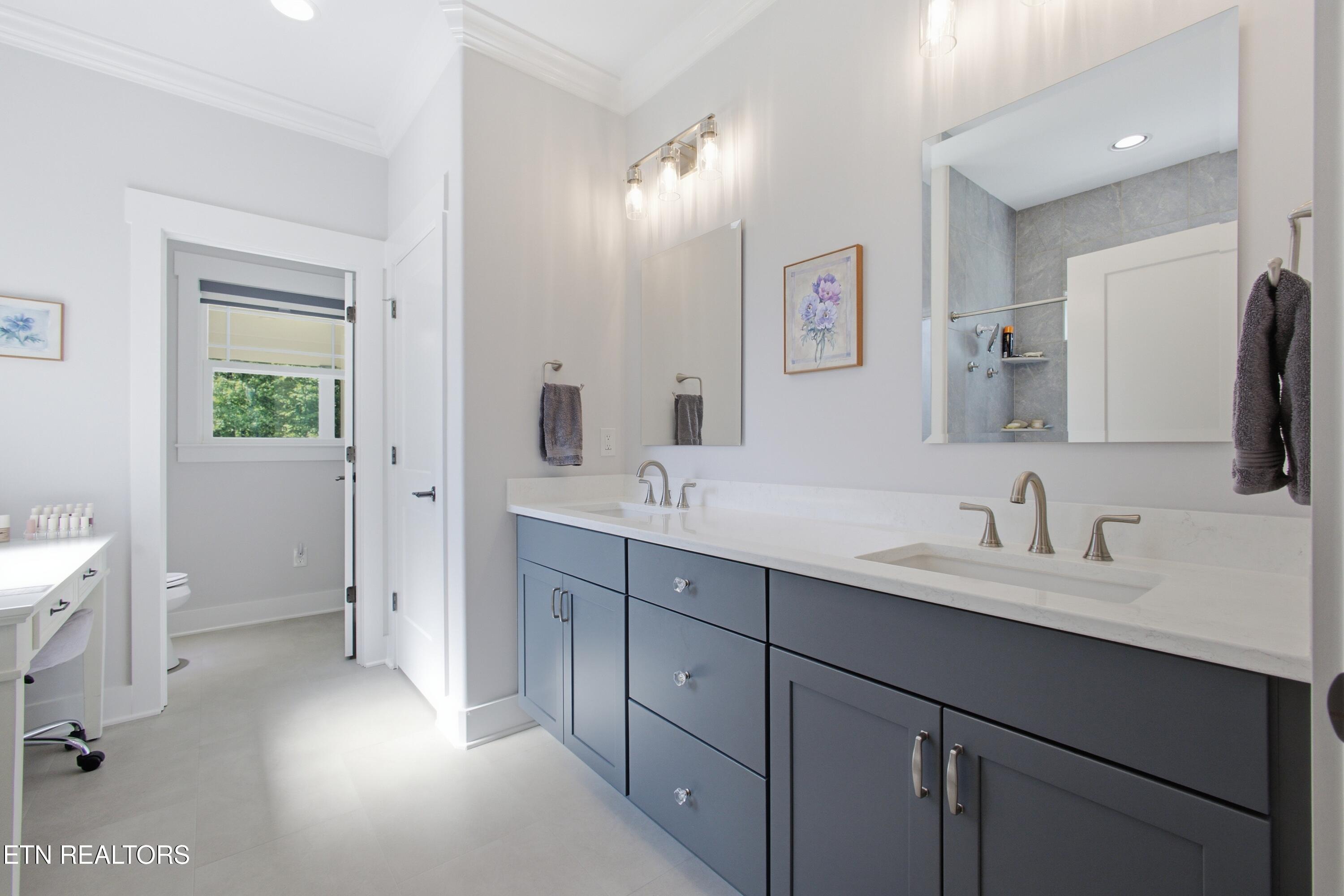 Bright bathroom with a double-sink vanity, dark cabinetry, and a tiled walk-in shower.