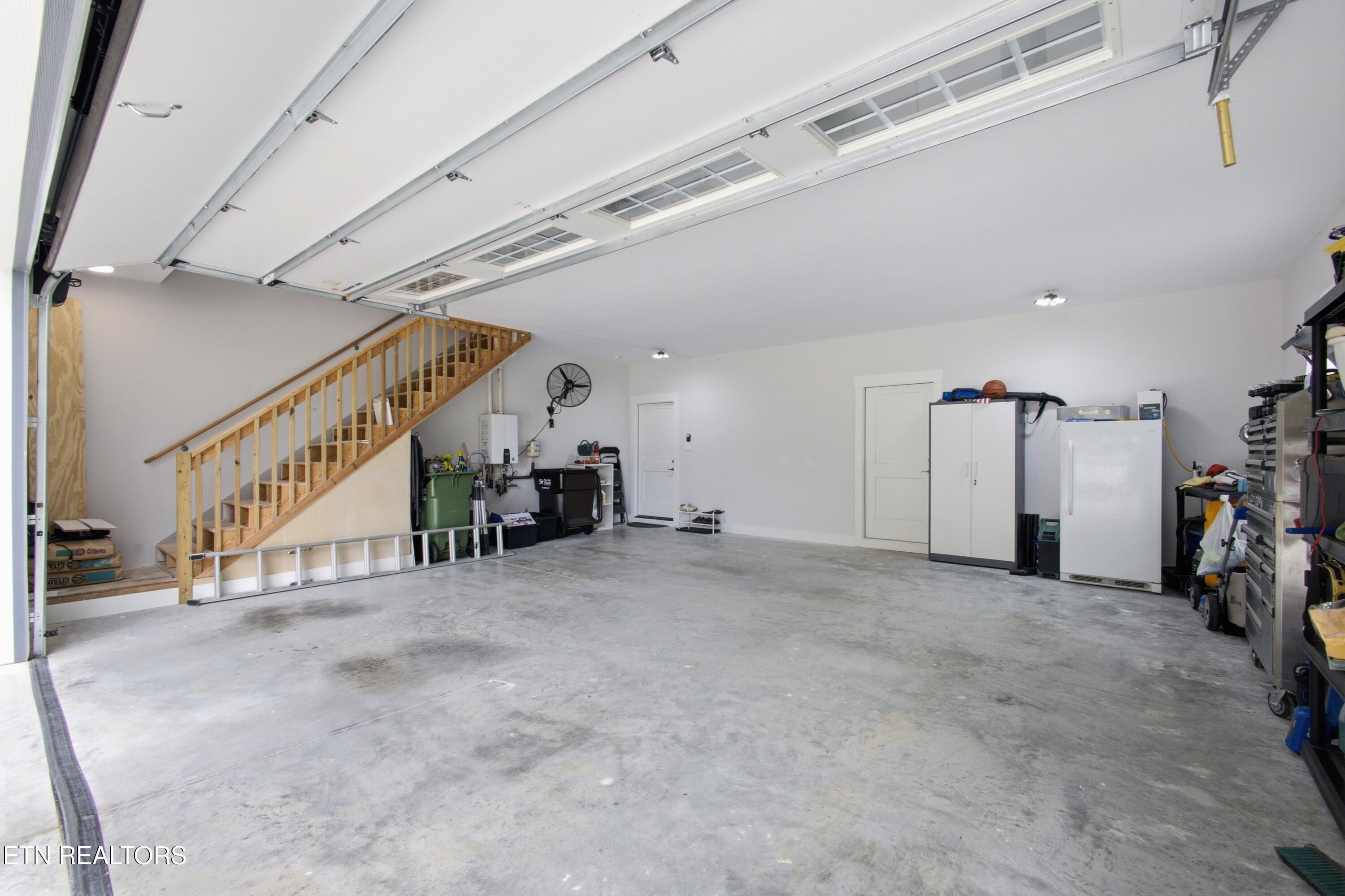 Spacious garage with a concrete floor, overhead door, and wooden staircase.