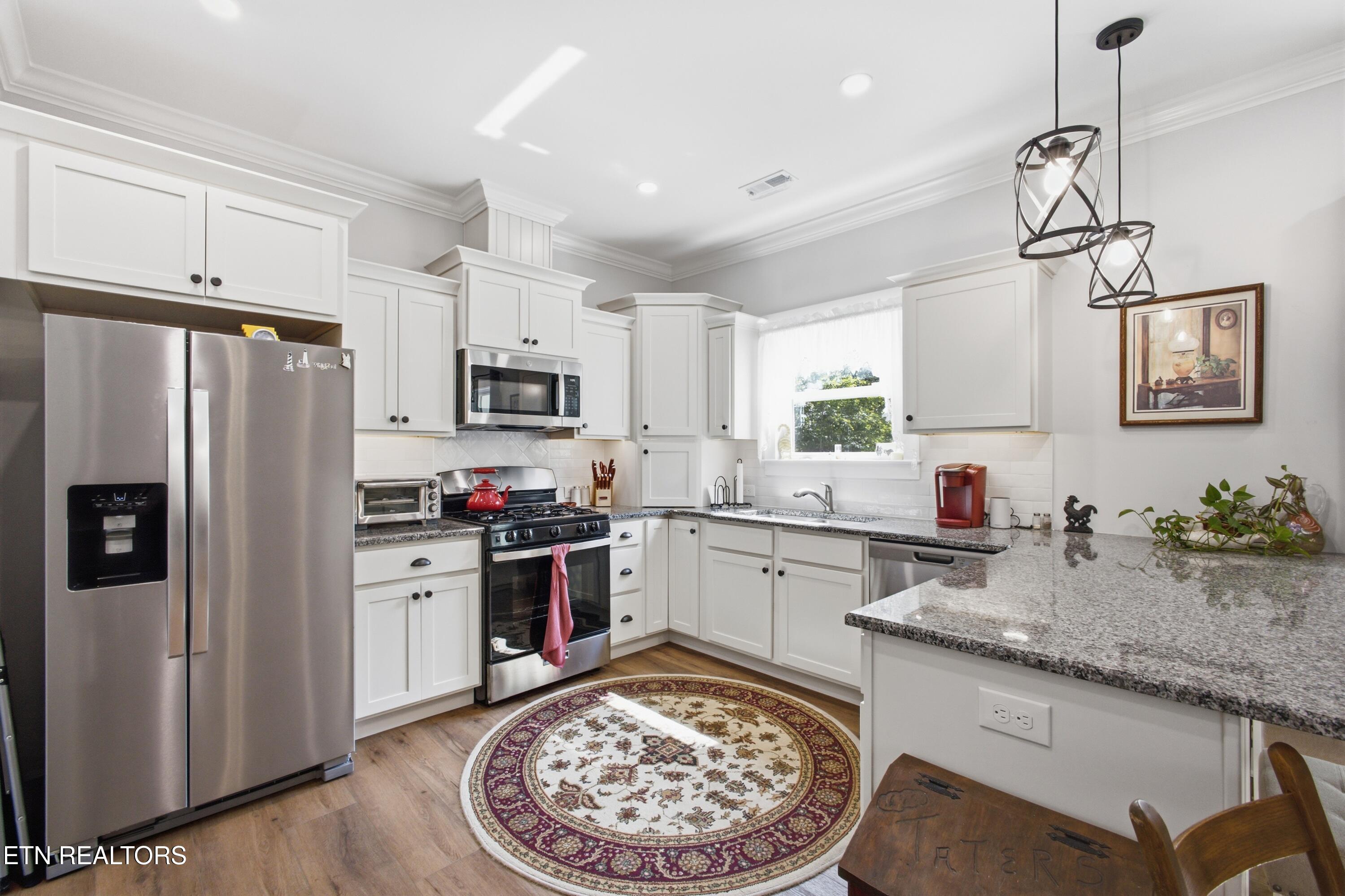 Bright kitchen with white cabinets, granite counters, stainless steel appliances, and a patterned round rug.