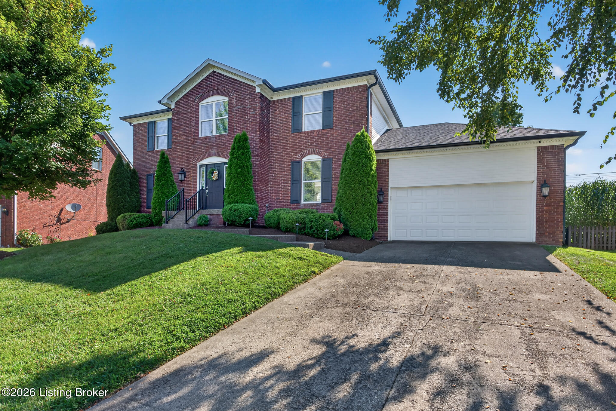 Two-story brick house with dark shutters, landscaped front yard, and attached two-car garage.