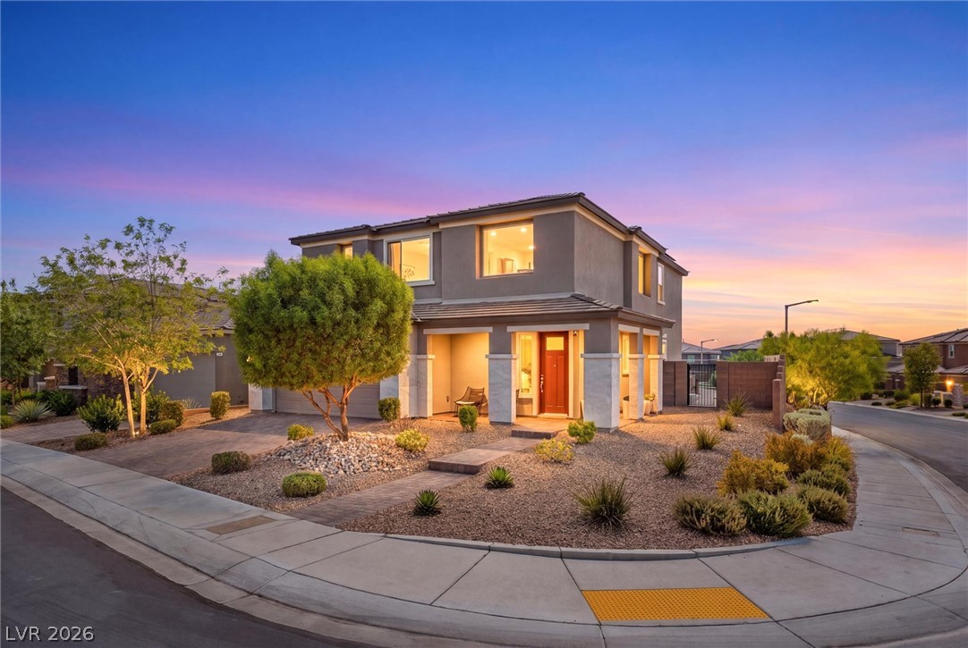 Two-story home with desert landscaping and warmly lit windows at dusk.