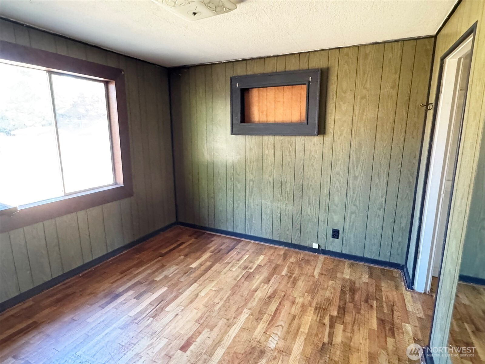 Empty room with wood-paneled walls, worn hardwood floors, and large and small windows.
