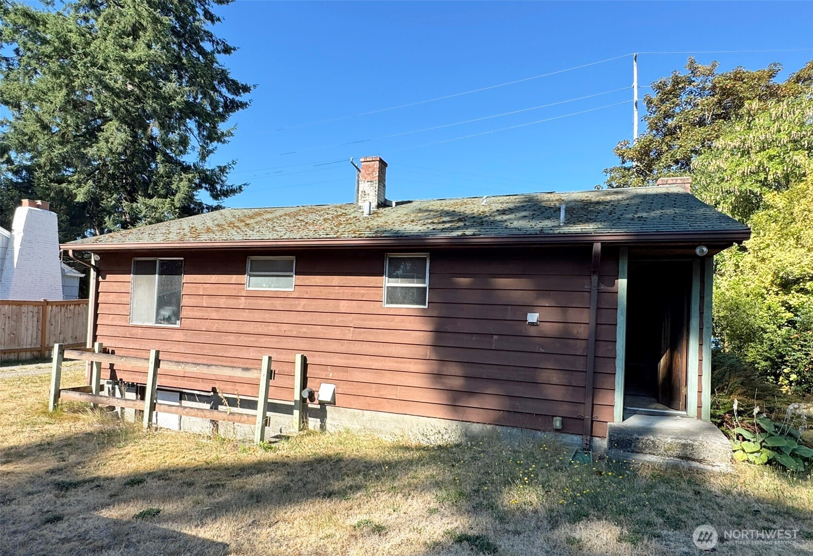 Brown-sided single-story house with a weathered roof and covered side entrance.
