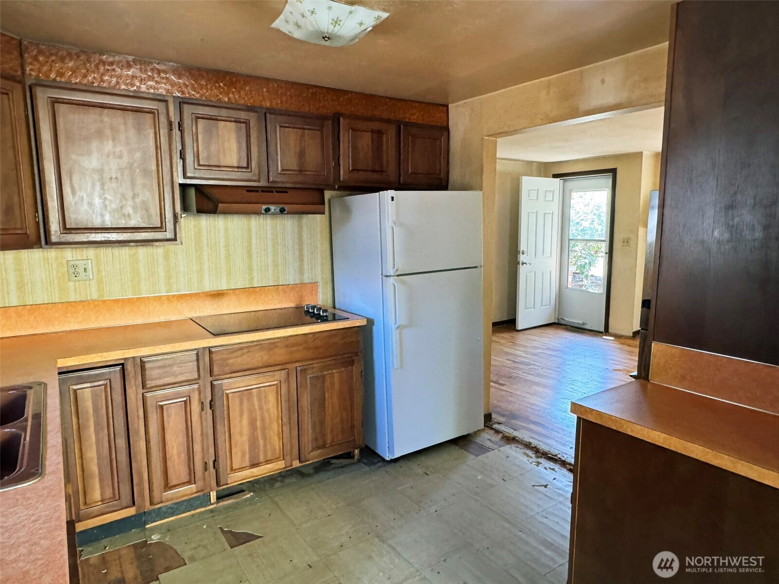 Kitchen with worn wood cabinets, a white refrigerator, and damaged flooring.