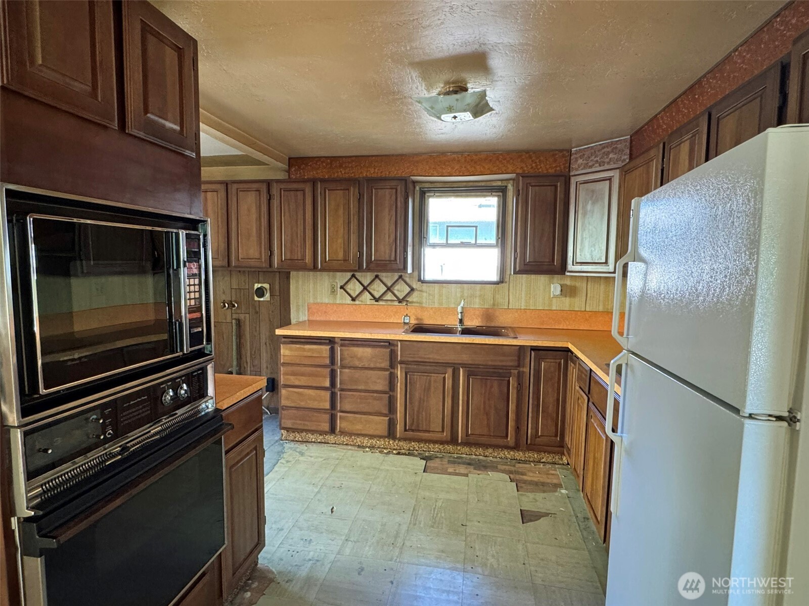 Kitchen with dark wood cabinets, orange countertops, built-in double oven, and worn flooring.