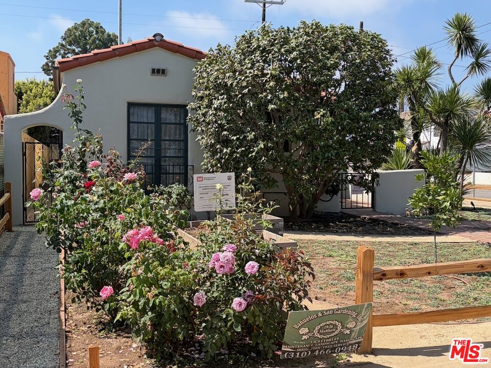 Spanish-style stucco home with a red tile roof, gated entry, and pink roses along the path.